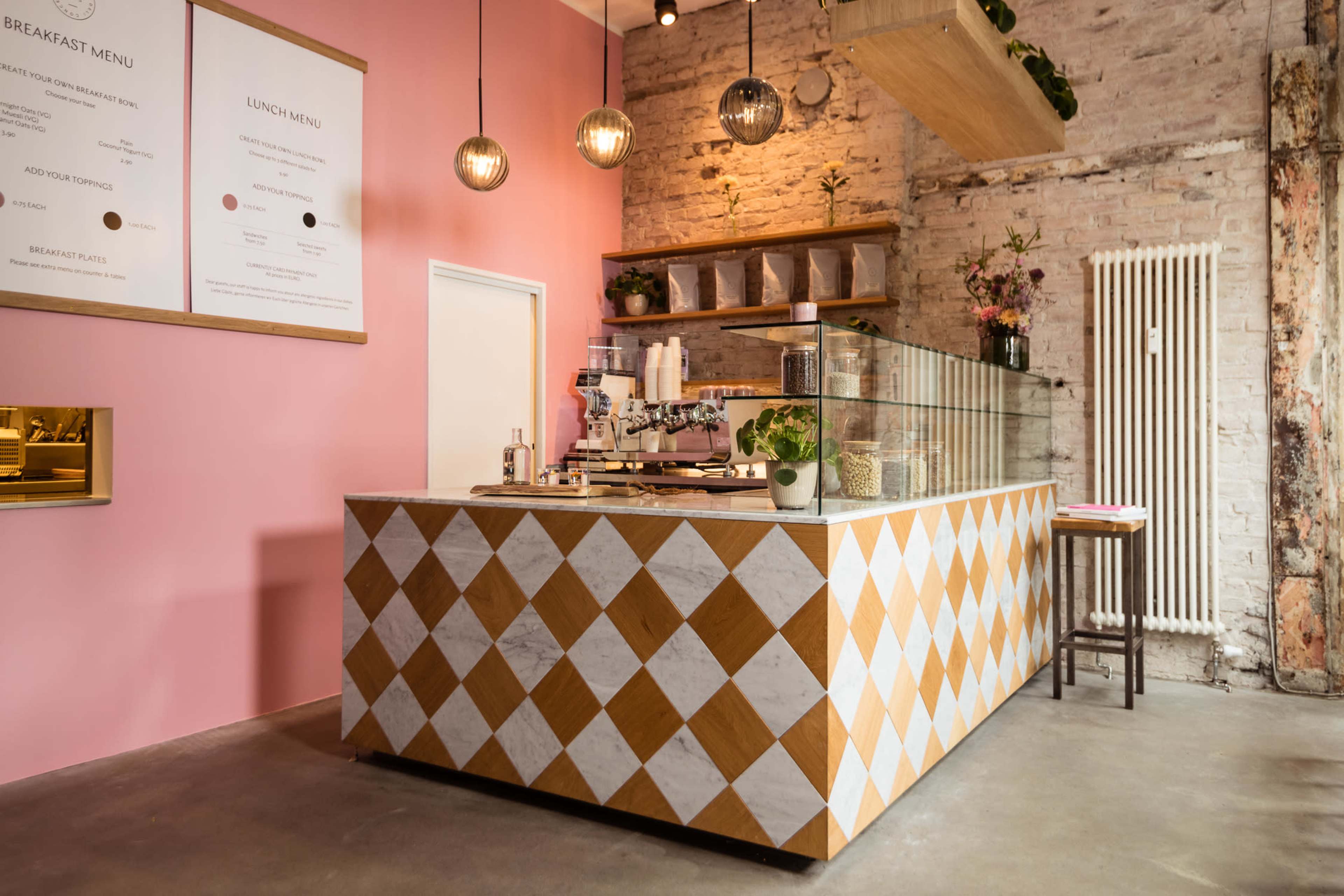 A cafe interior with a colorful diamond-patterned counter, light pink walls, and decorative lighting fixtures.