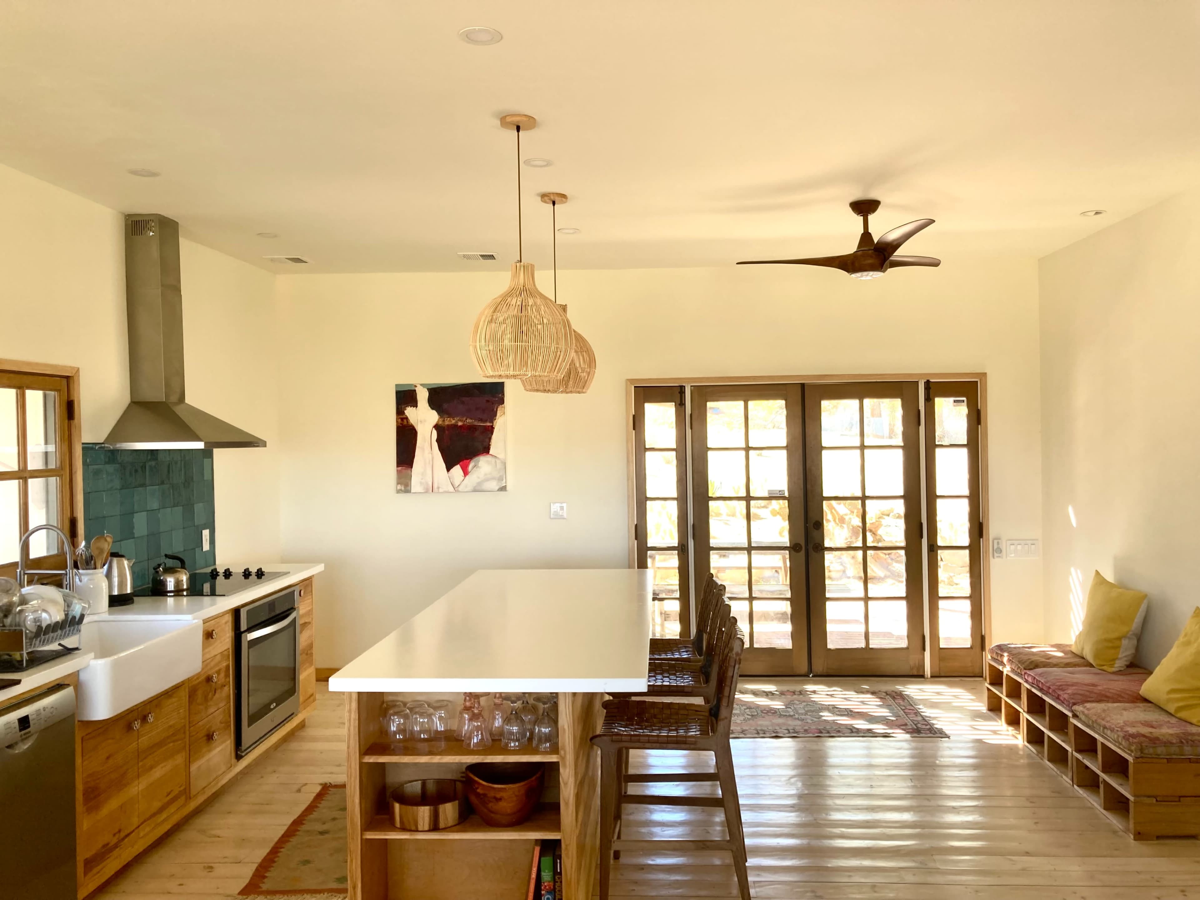 The image shows a modern kitchen with a large island, wooden cabinetry, and a set of double doors leading to an outdoor area.