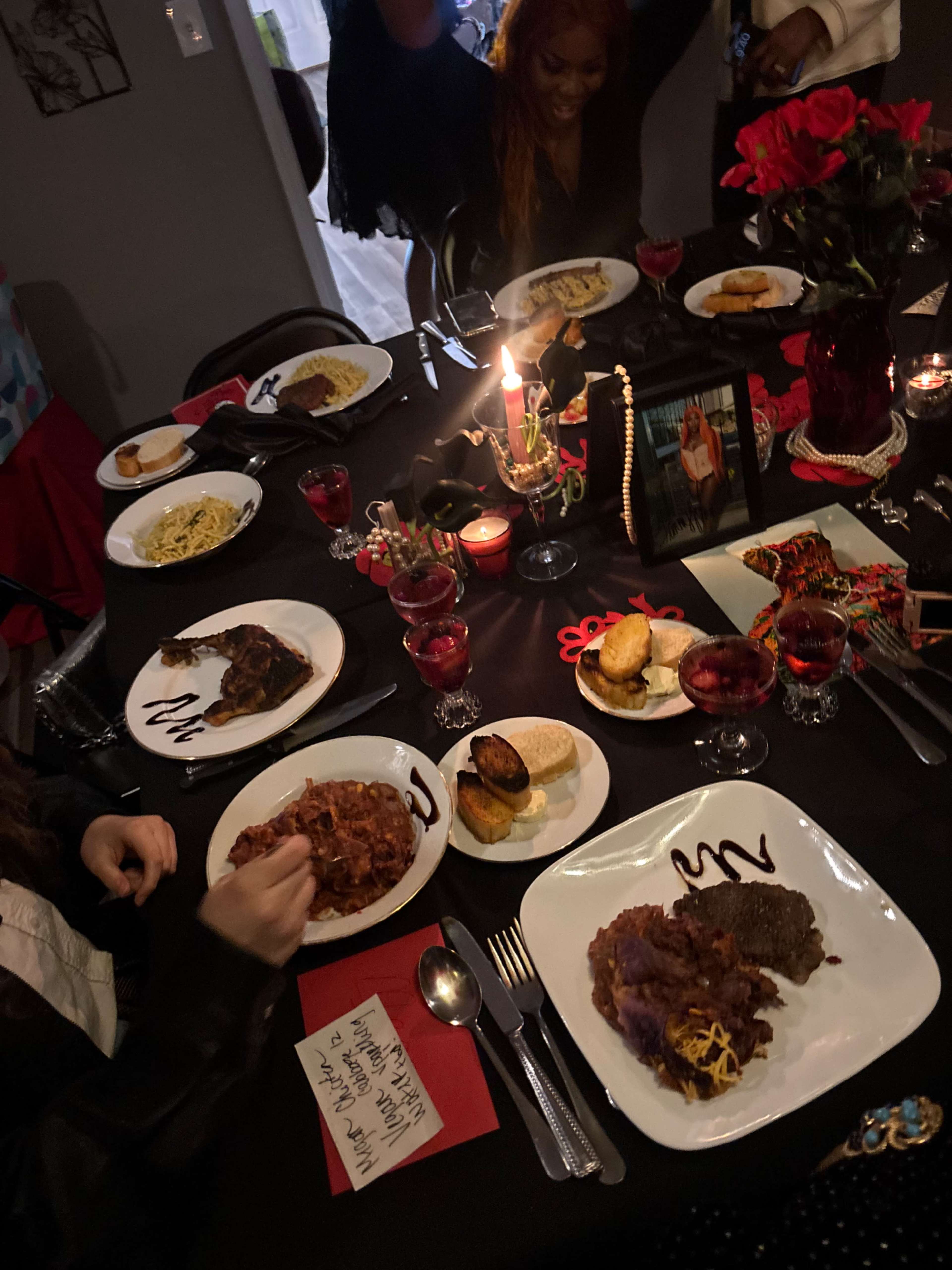 A dinner table is set with various dishes including pasta, meat, and desserts, surrounded by candles and decorations.