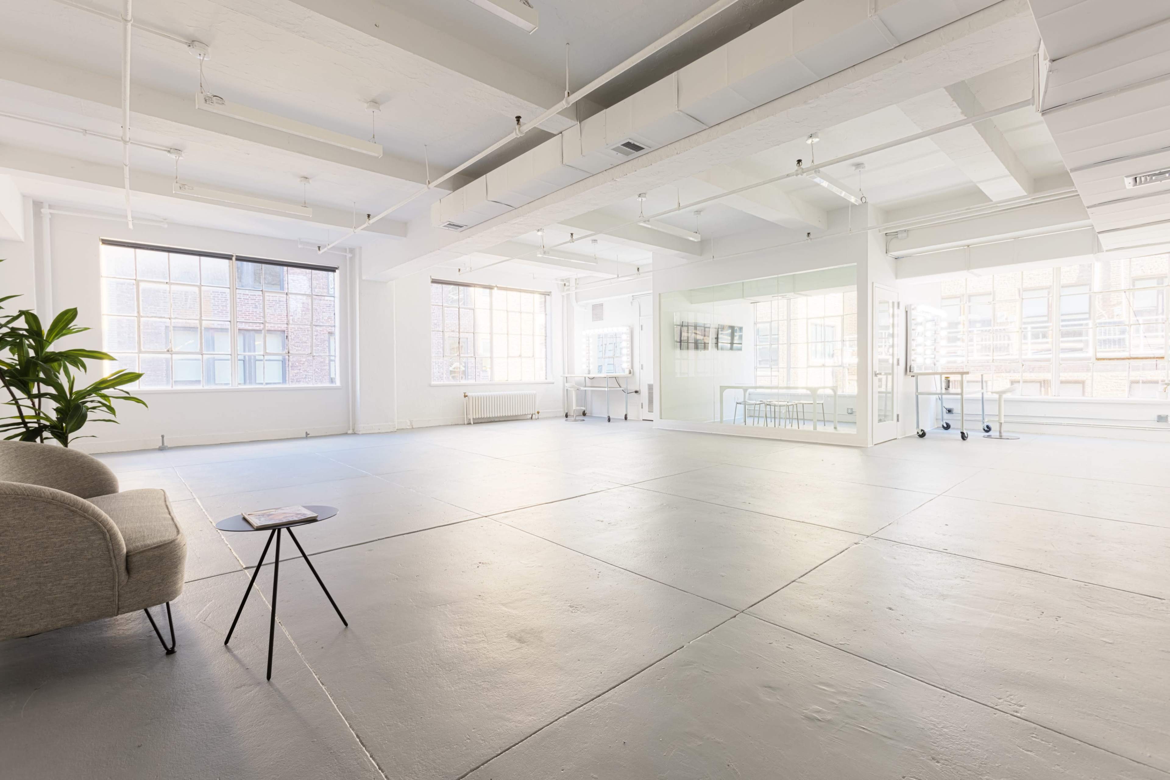 A spacious, well-lit room with large windows, a small table, and a couch in one corner.