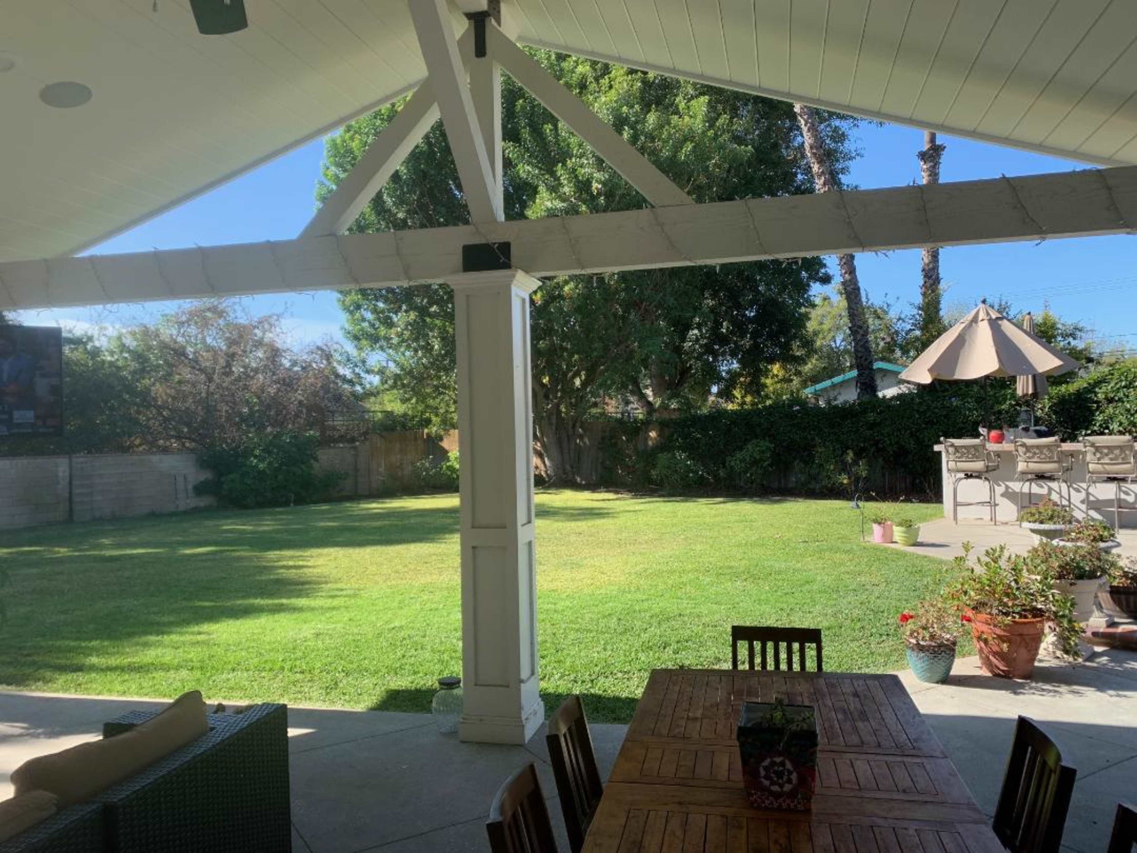 A spacious backyard with a well-maintained lawn, a shaded patio area, and a dining table underneath a pergola.