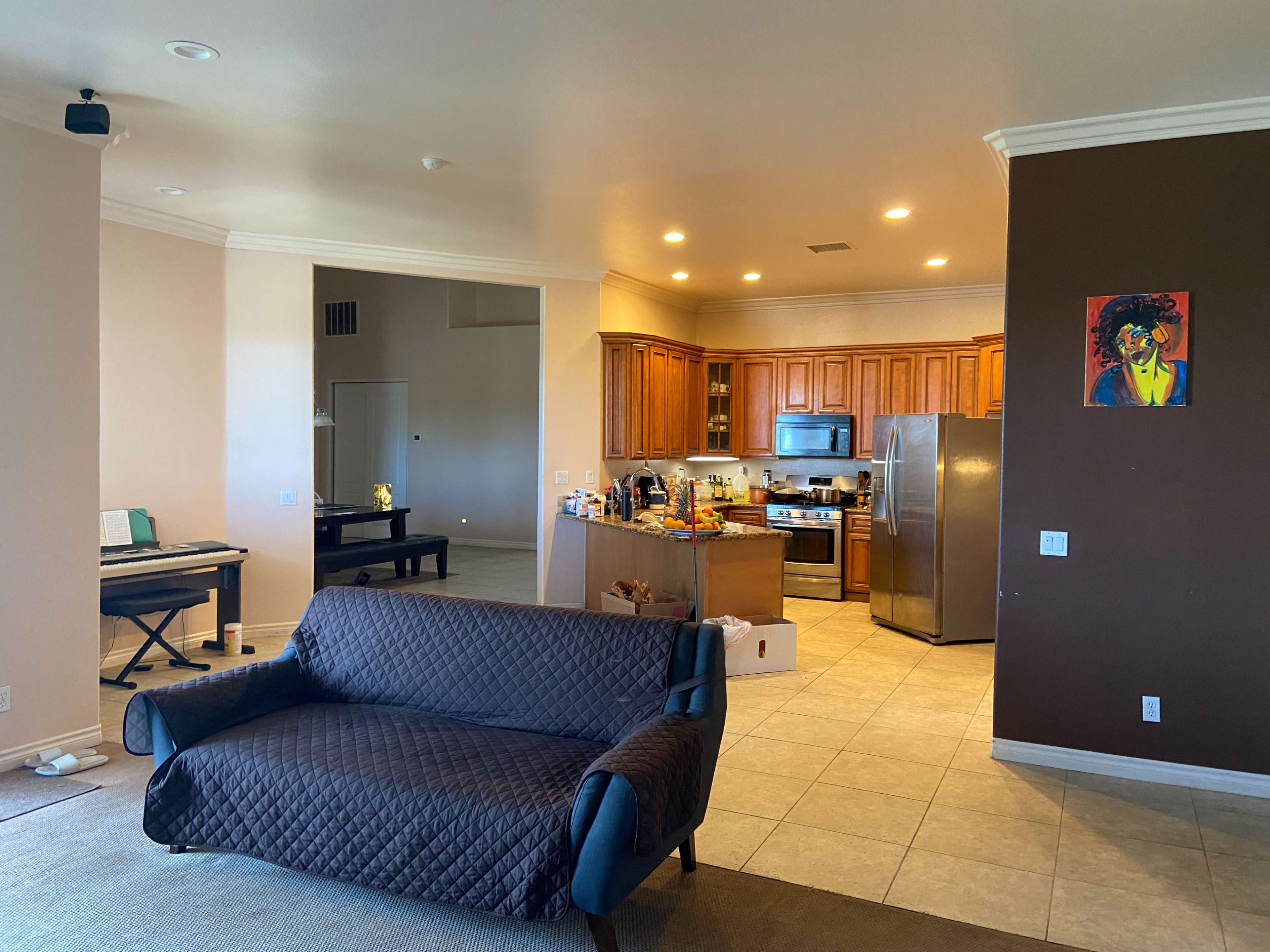 A spacious living area features a sofa facing a kitchen with wooden cabinets and various items on the counter.