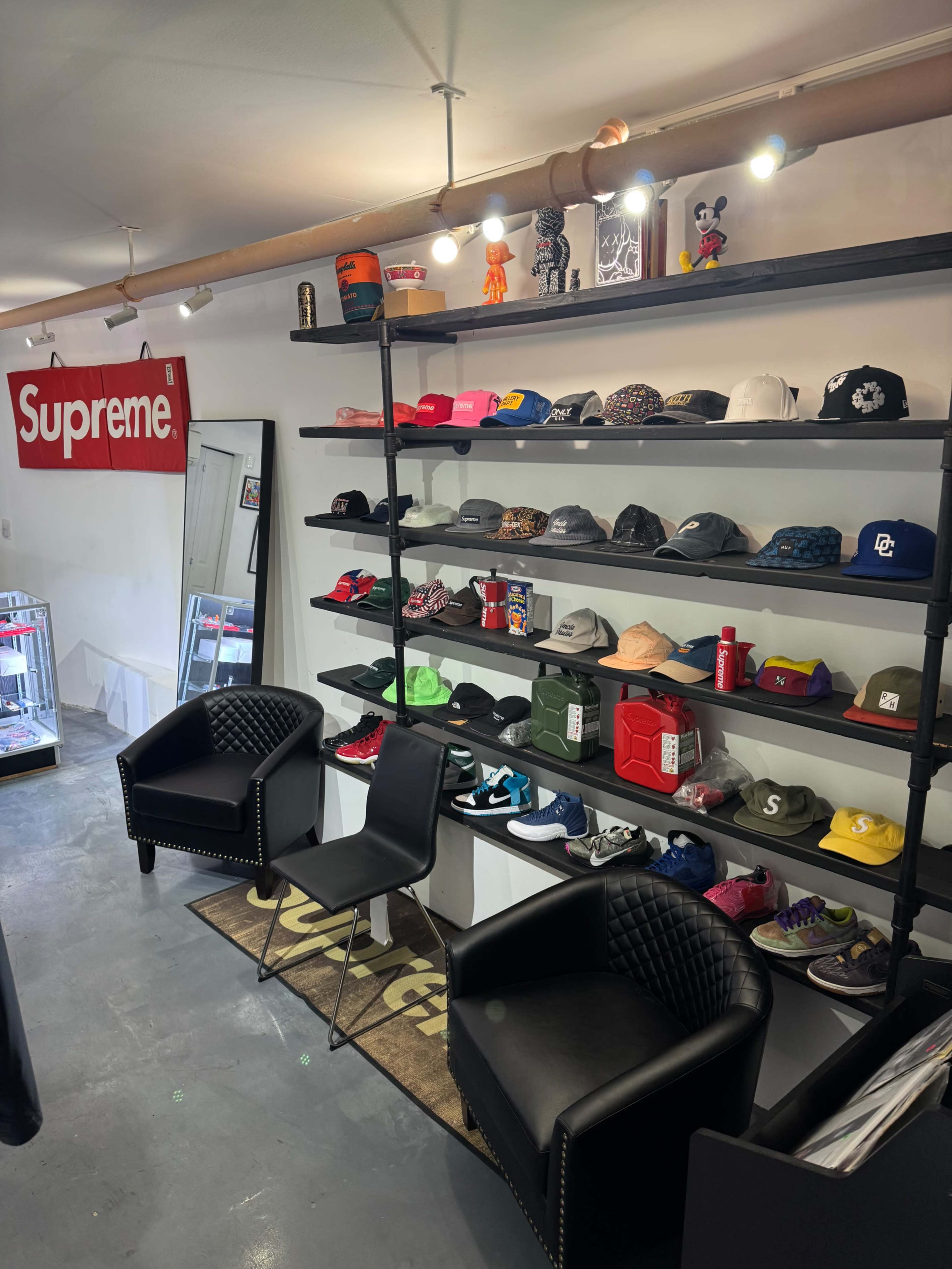 The image shows a retail space with shelves displaying various hats and accessories, along with a seating area featuring two black chairs.