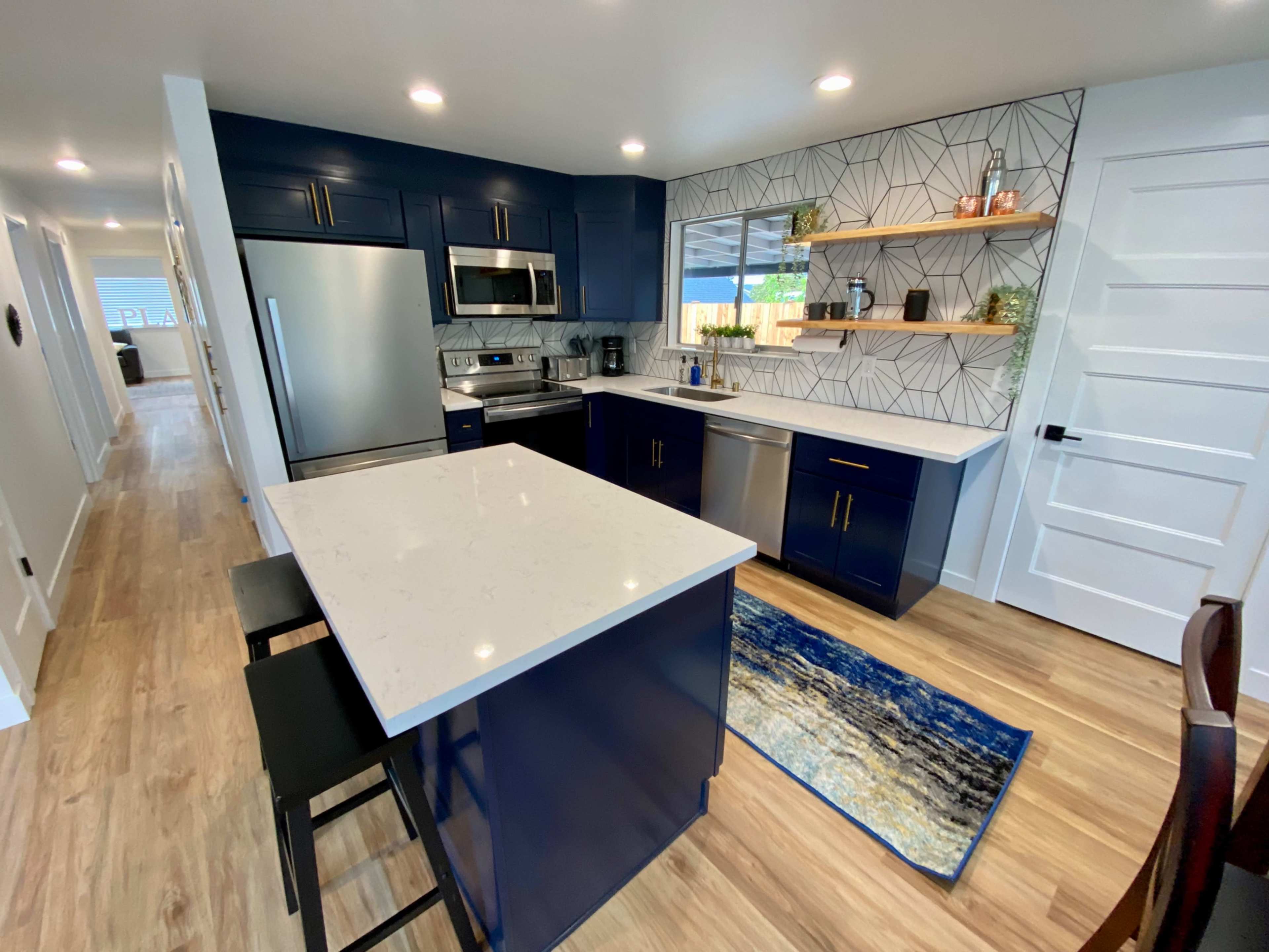 A modern kitchen features dark blue cabinets, stainless steel appliances, and a large white countertop with wooden shelves and decorative items.