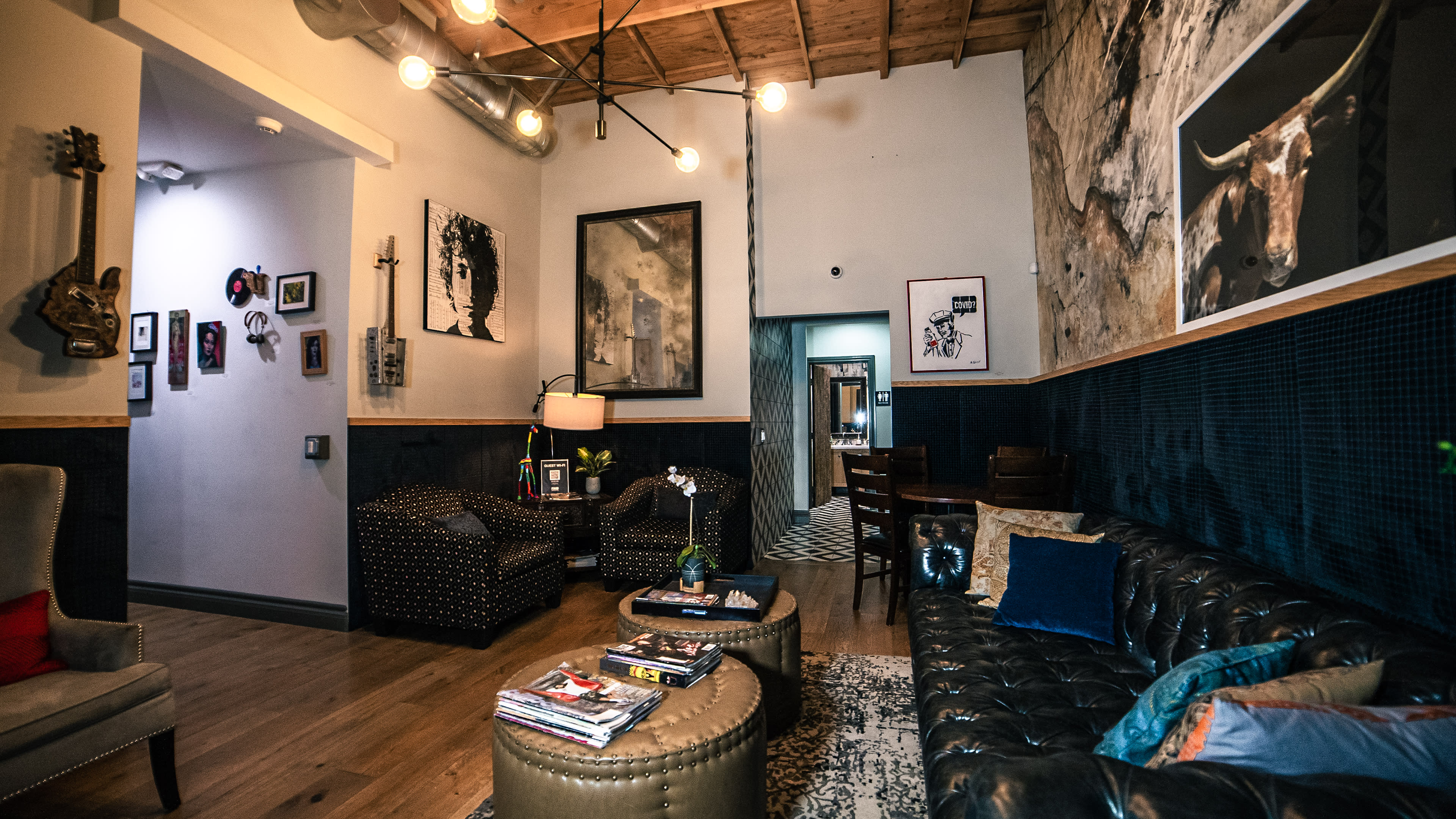 The image shows a well-decorated lounge area featuring a leather sofa, patterned chairs, artwork on the walls, and warm lighting fixtures hanging from the ceiling.