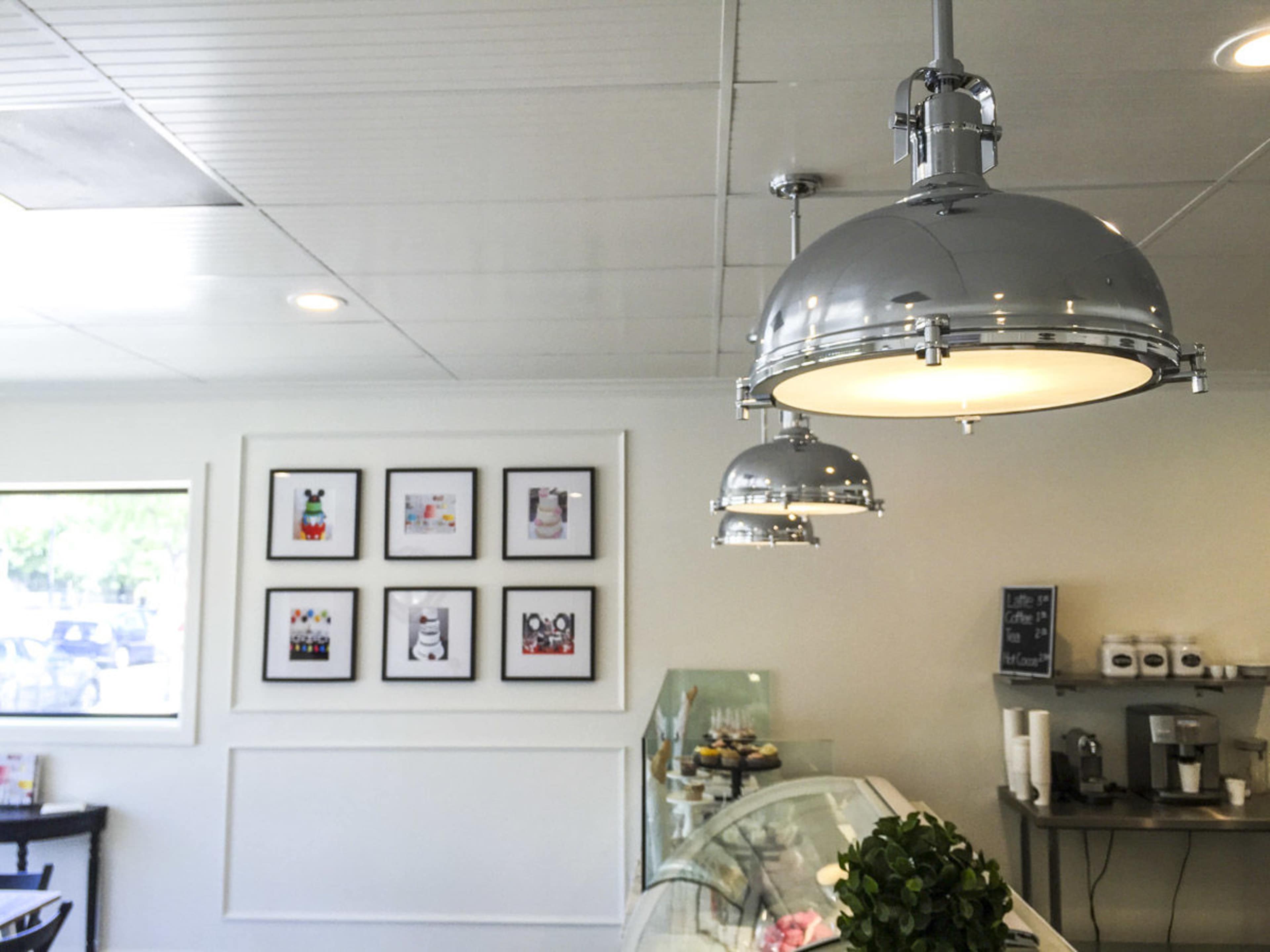 A brightly lit café interior with chrome pendant lights and framed artwork on the wall, alongside a display of pastries.