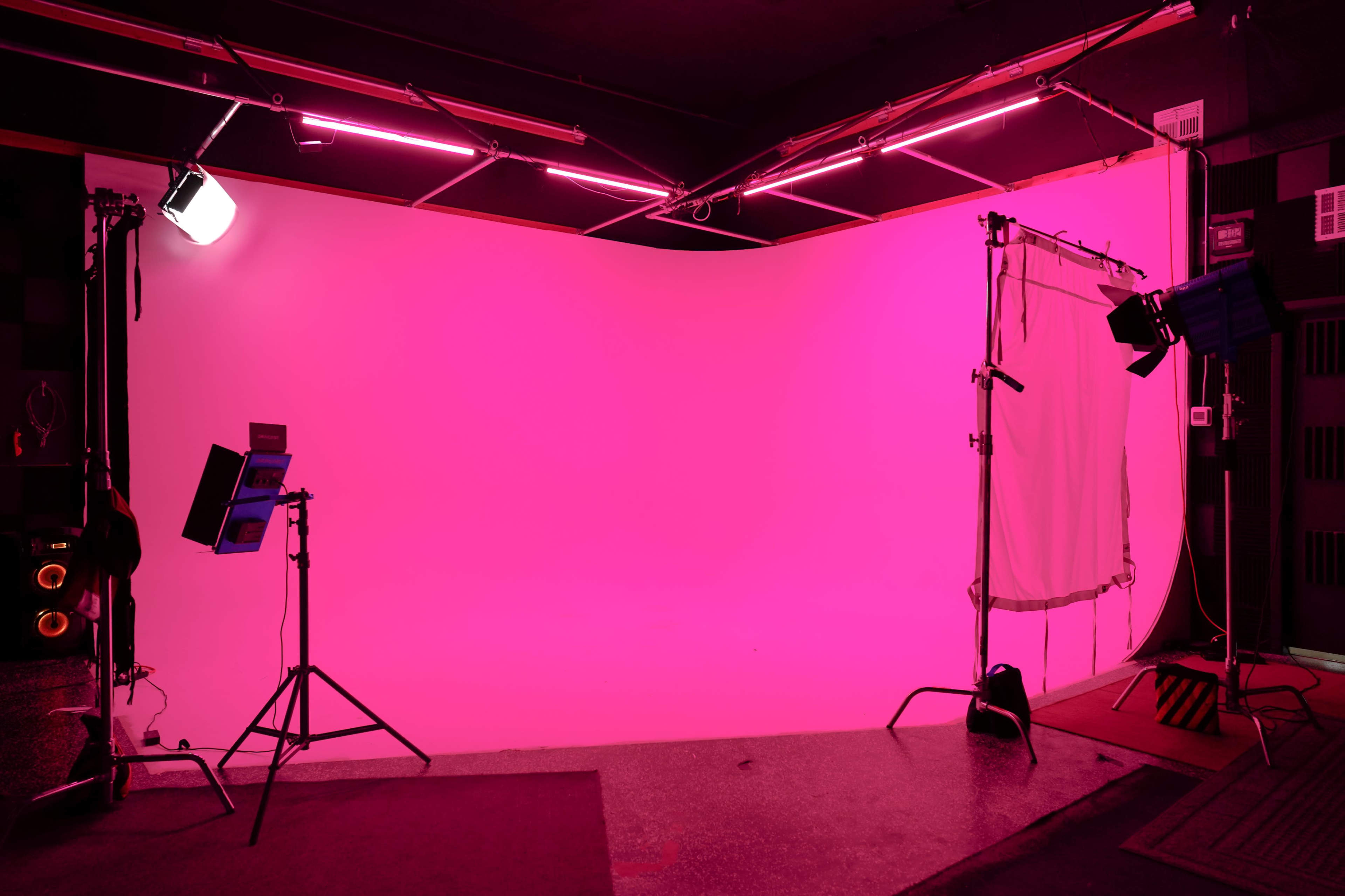 A photography studio features a brightly lit pink backdrop, with studio lights and equipment arranged around the space.