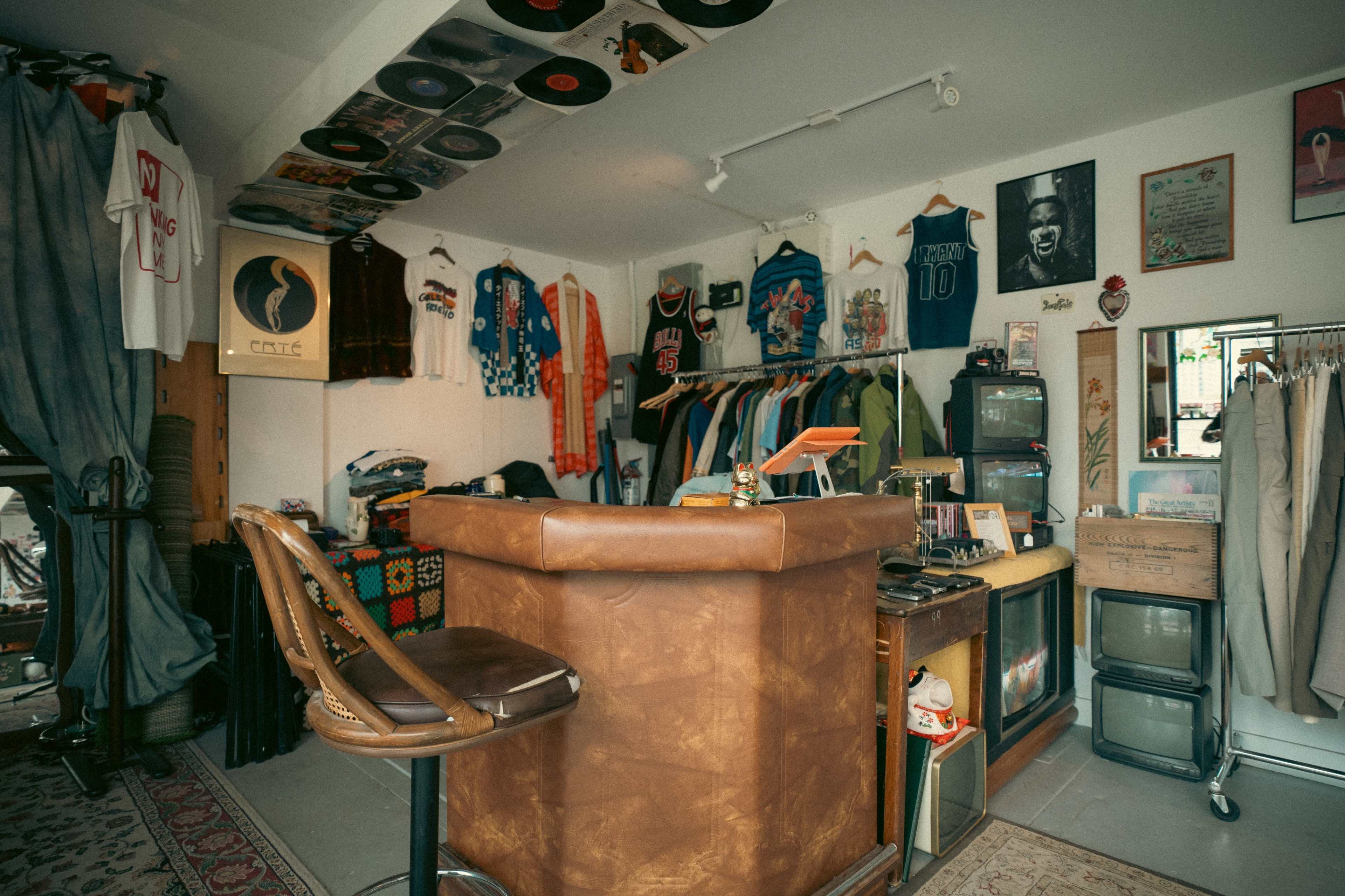 The image features a vintage clothing shop interior with a bar-like counter, racks of clothes, and various memorabilia displayed on the walls and shelves.