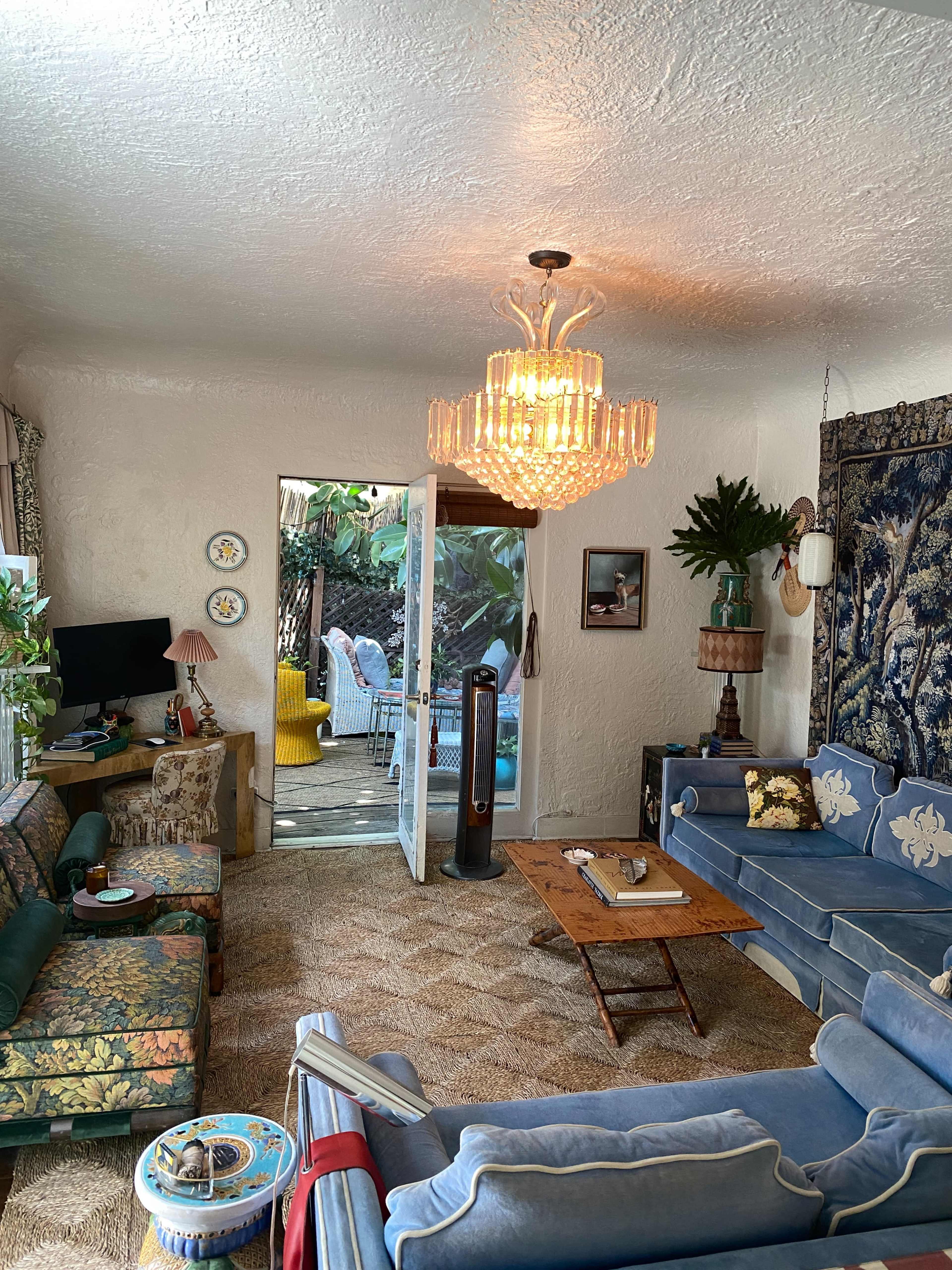 A cozy living room with patterned sofas, a chandelier, and a view of an outdoor area through an open door.