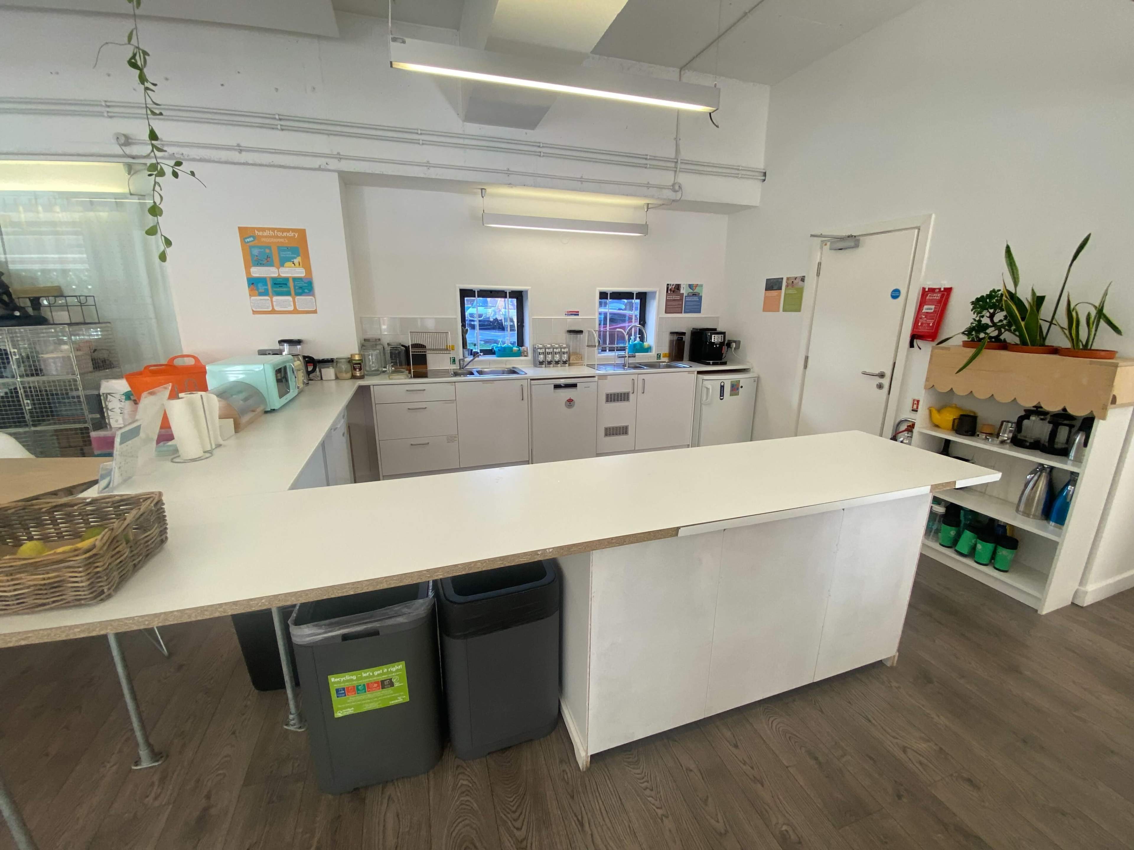 A modern kitchen area with white countertops, storage cabinets, coffee machines, and a variety of kitchen appliances arranged neatly.