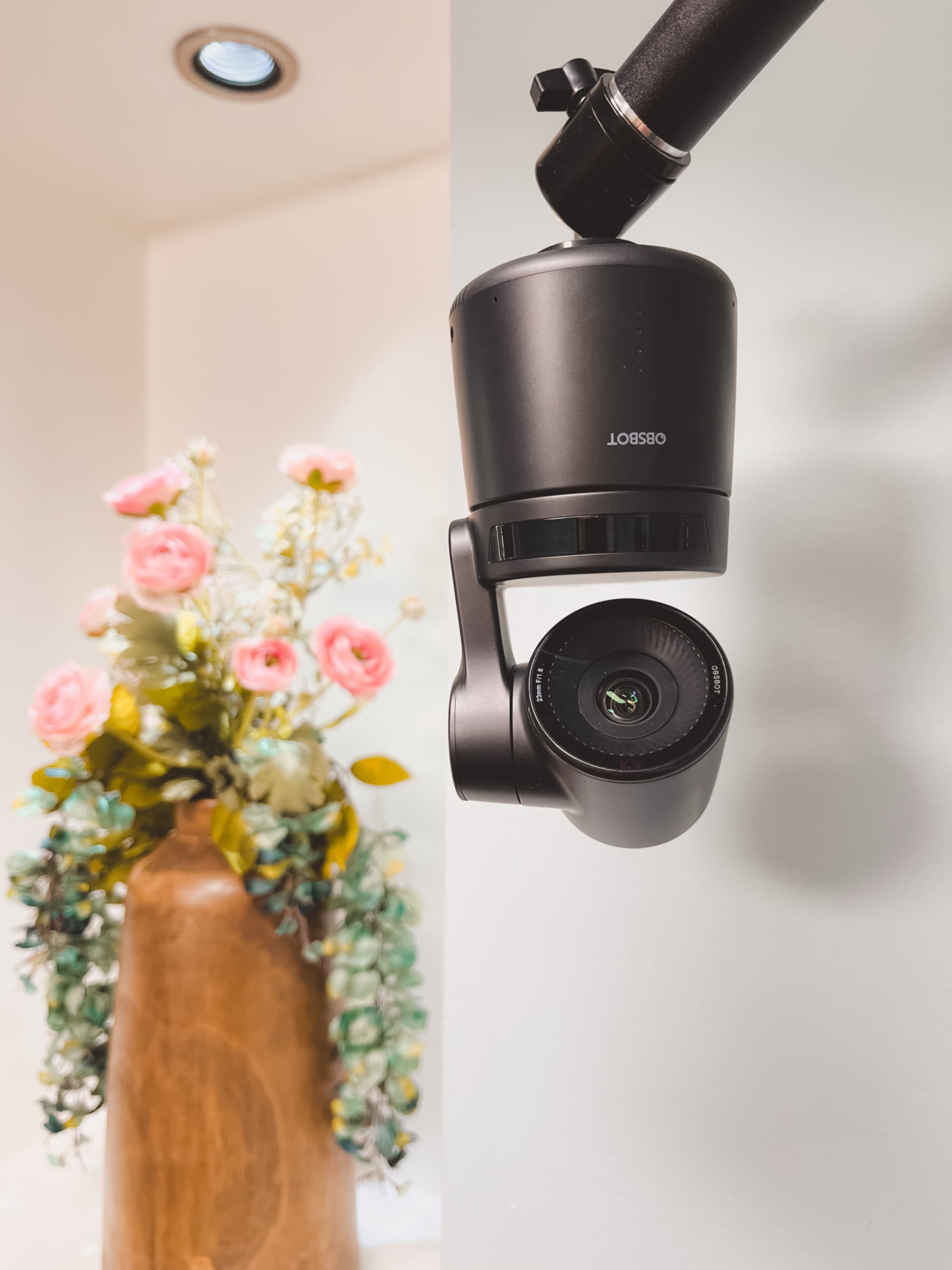 A camera hangs from a ceiling mount, positioned near a vase of pink flowers and greenery.