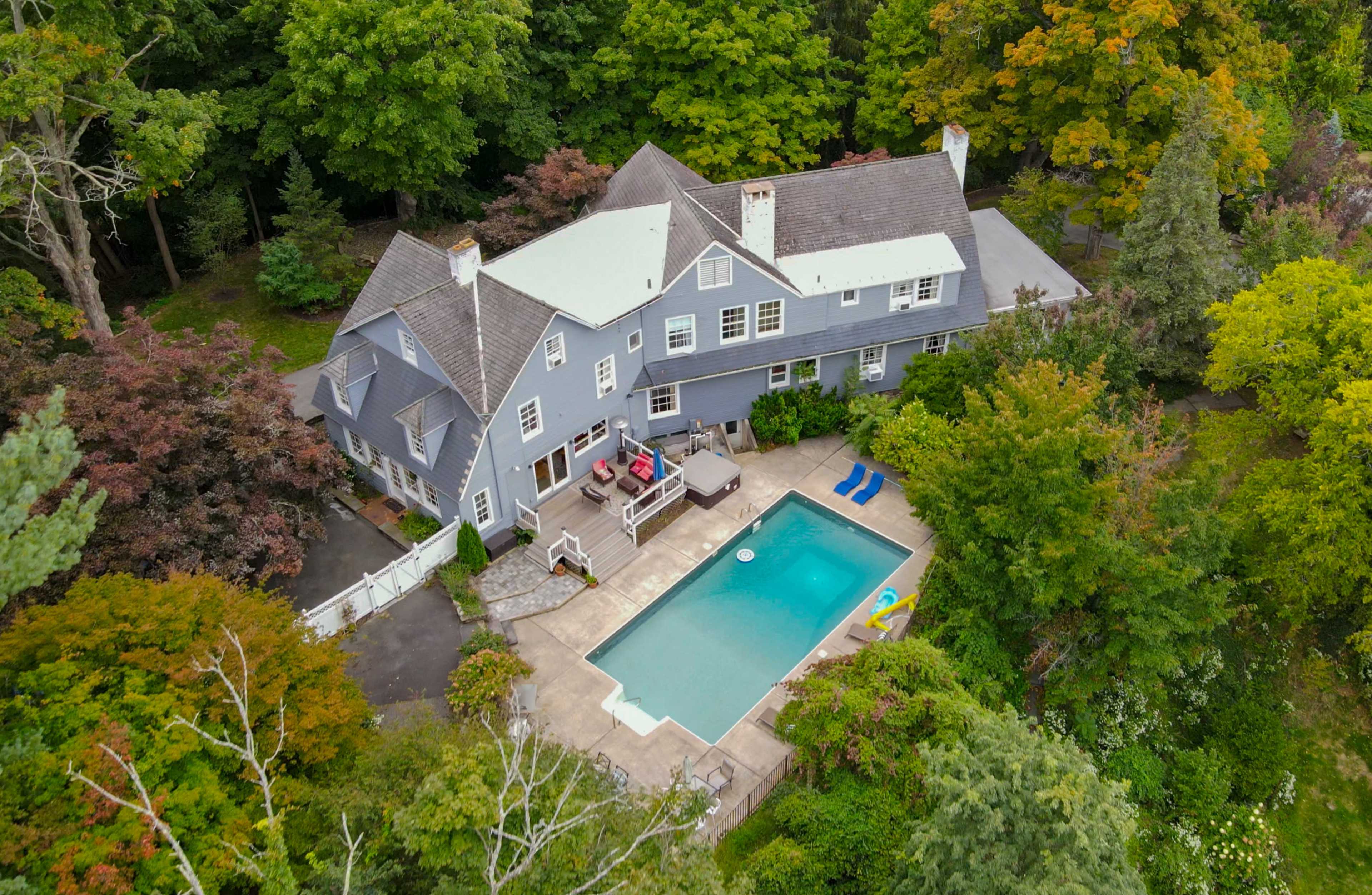 A spacious blue house with a swimming pool is surrounded by trees and colorful foliage.