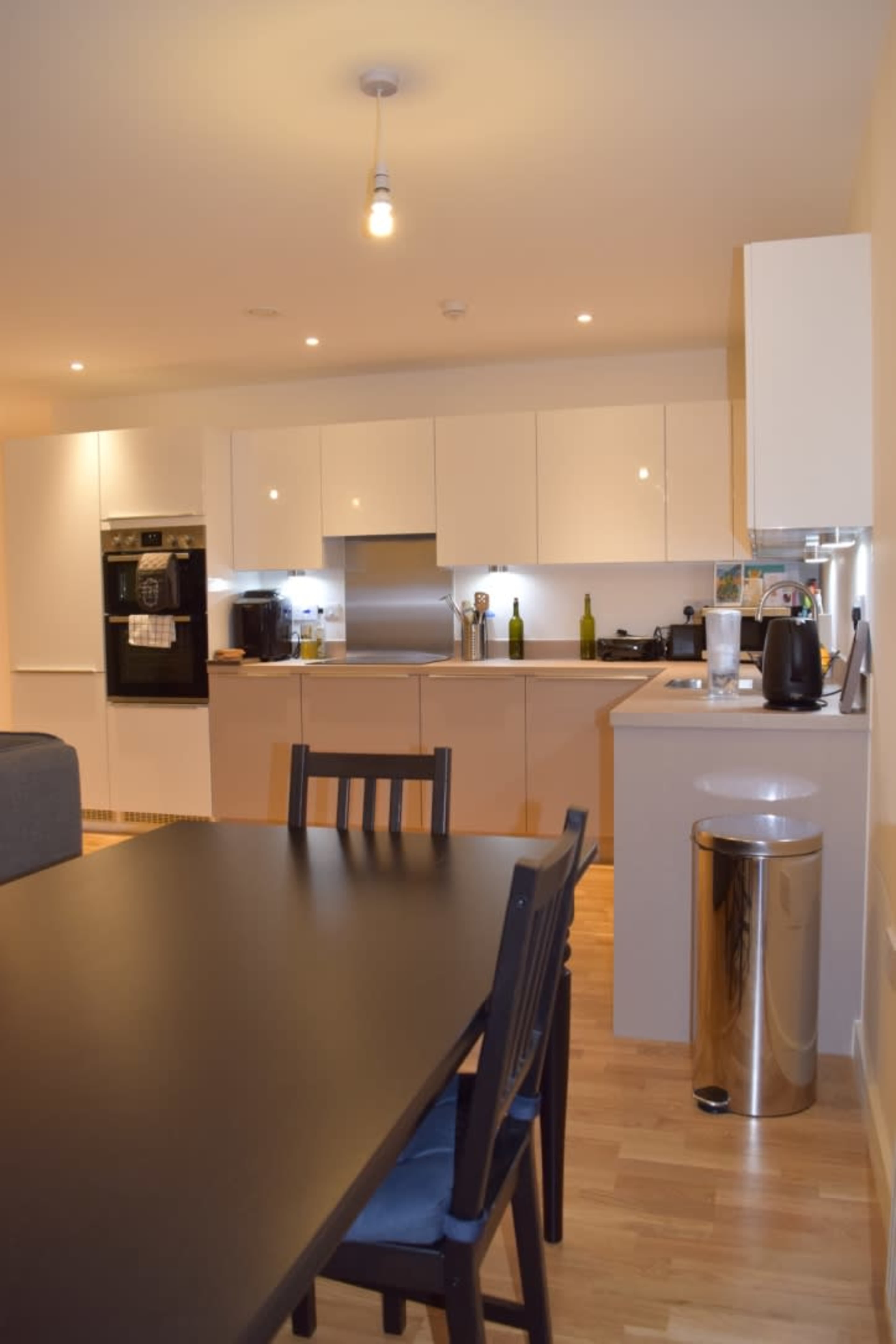 The kitchen features modern cabinetry, appliances, and a dining table nearby.