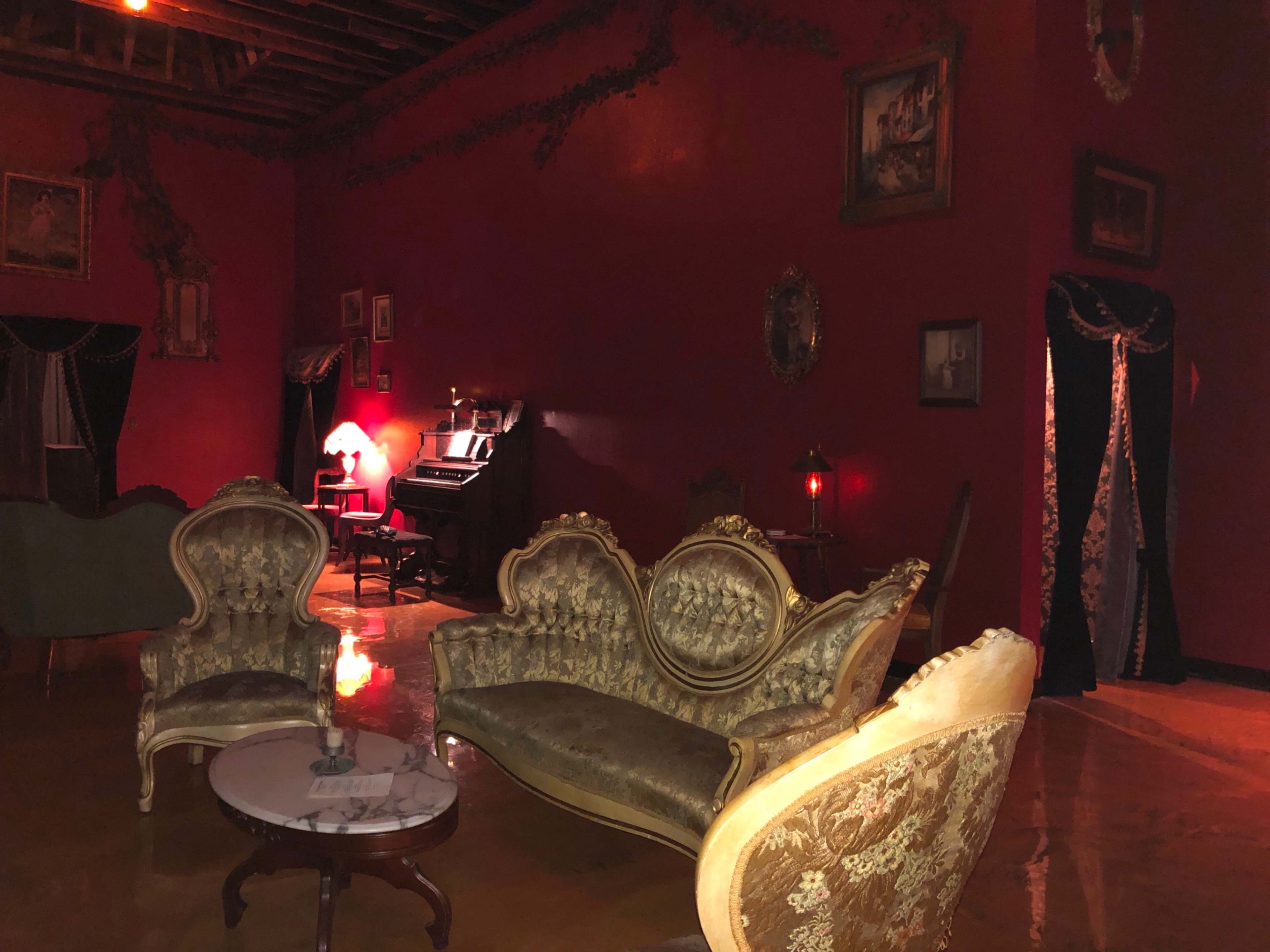 The image shows a vintage sitting room with ornate furniture, a piano, and a warmly lit atmosphere.