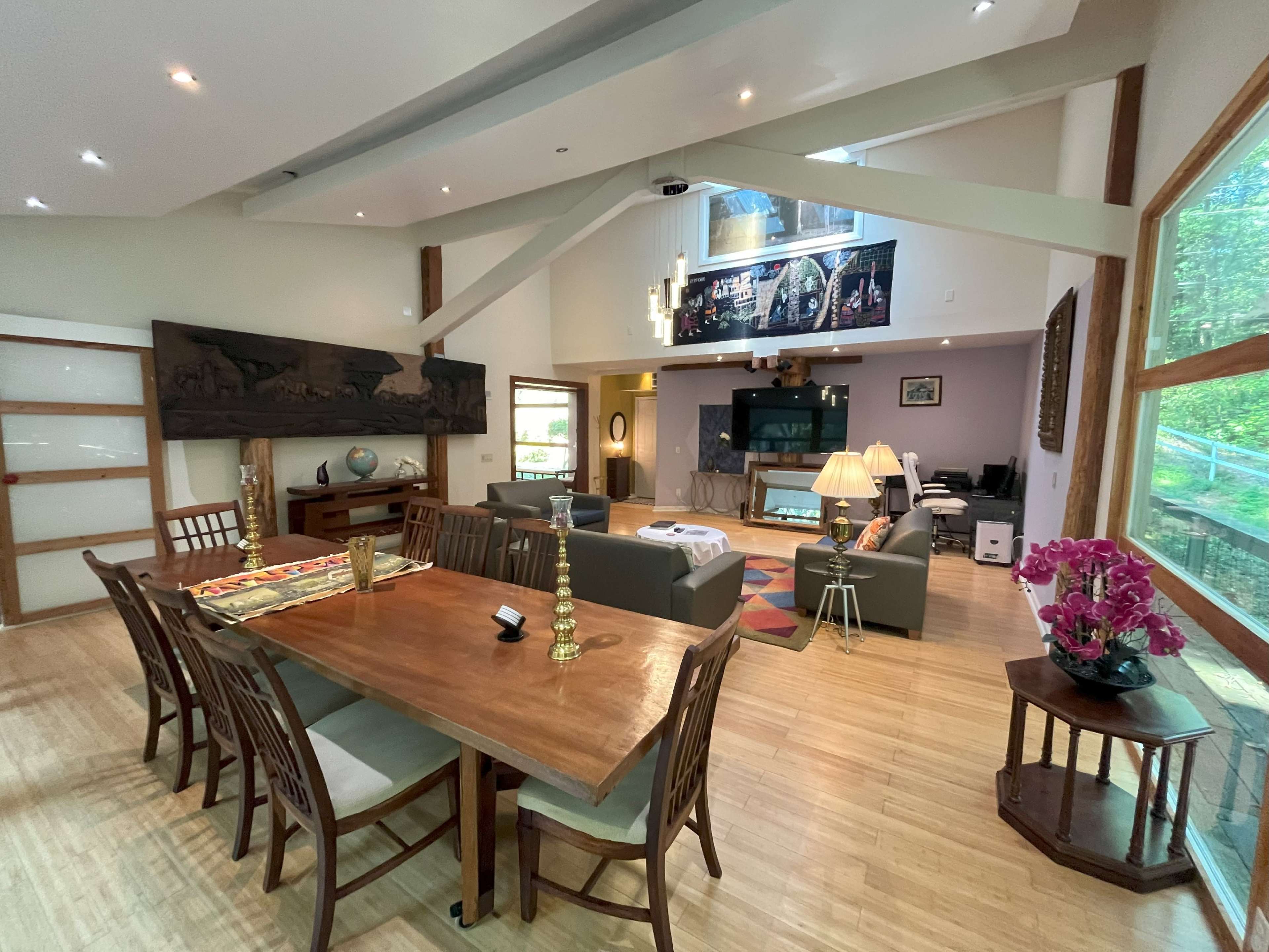 A spacious, modern living and dining area with a wooden dining table, comfortable seating, and large windows allowing natural light in.