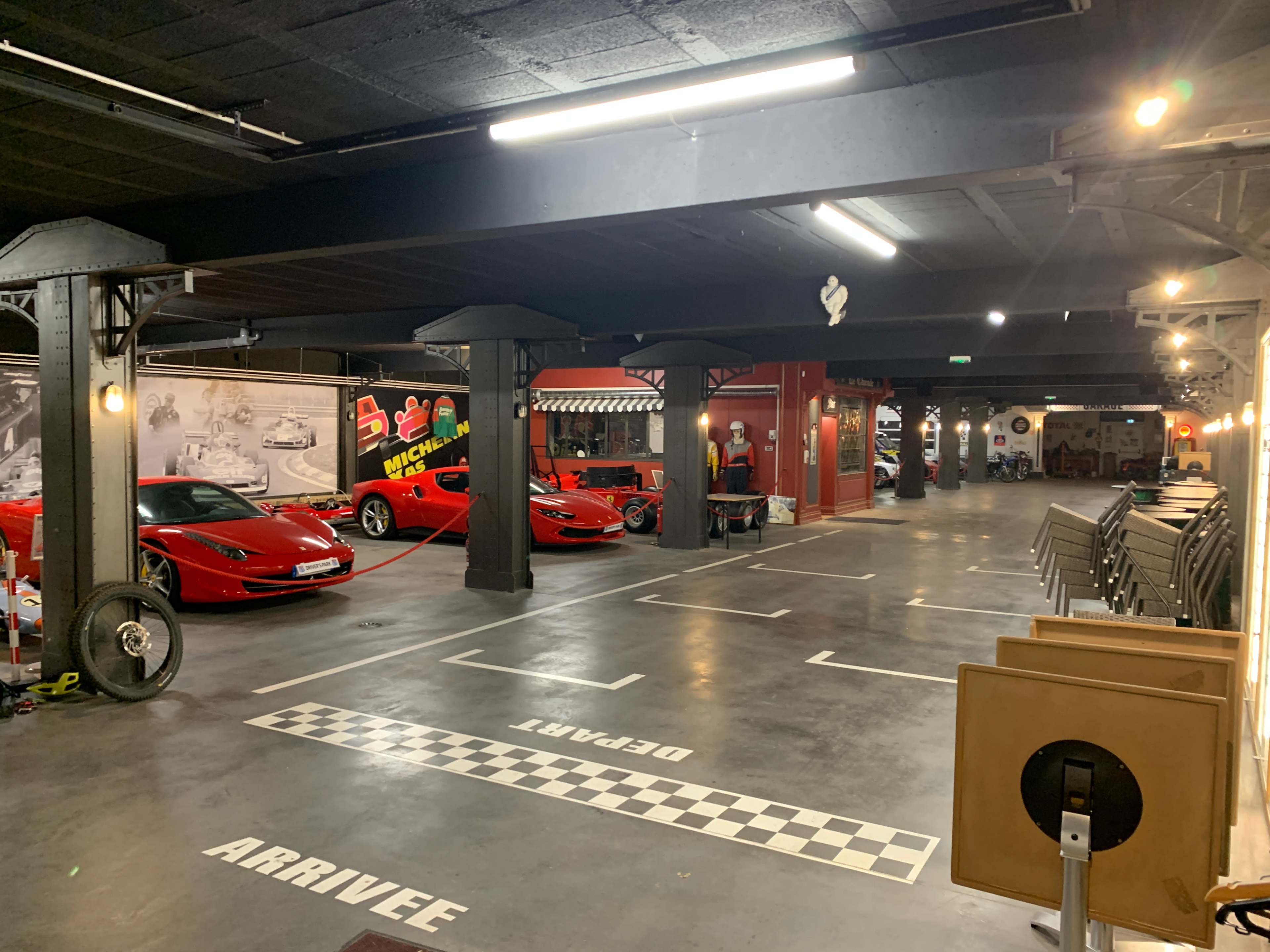 The image shows a spacious garage filled with multiple red sports cars, featuring a checkered floor design and various decorations along the walls.