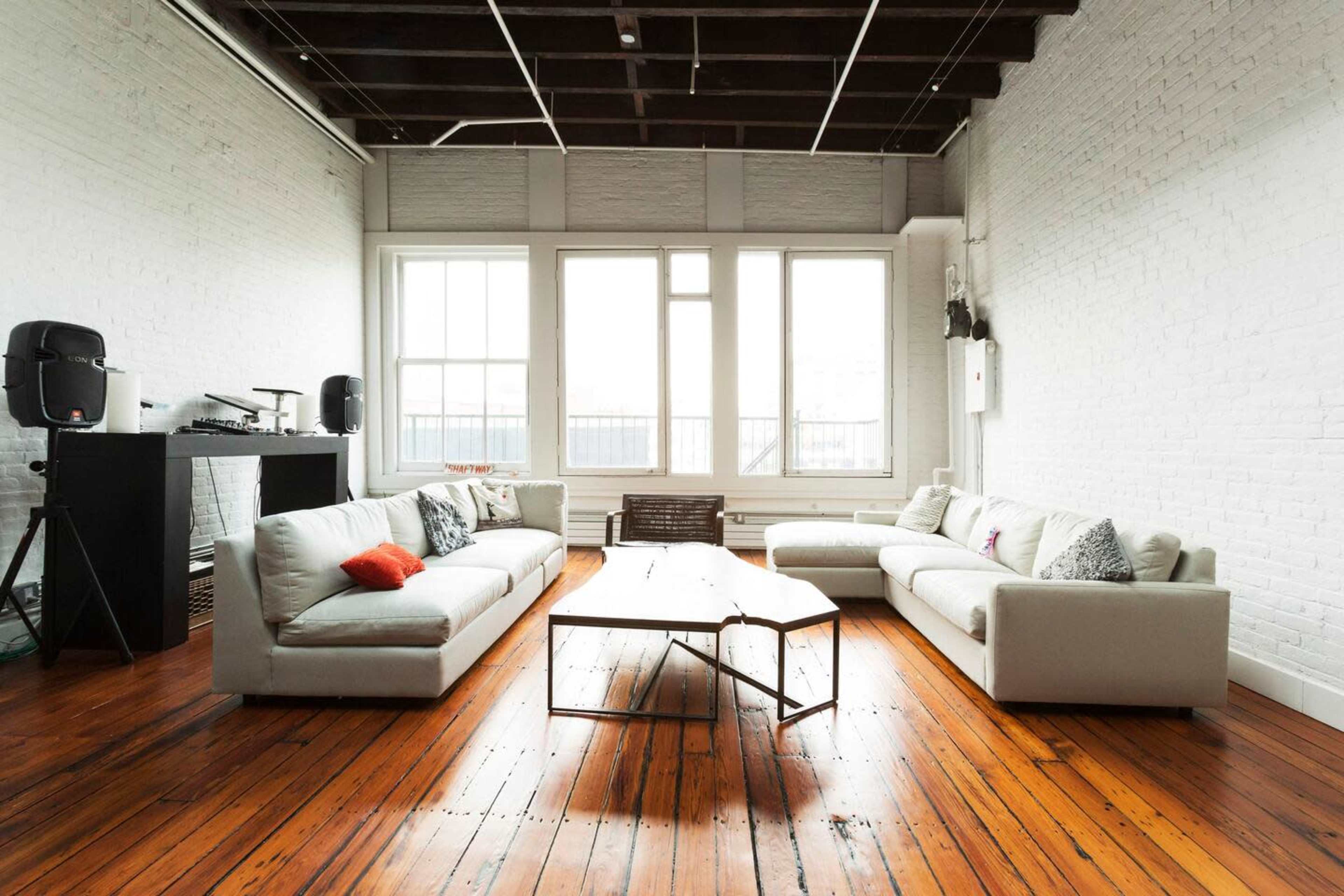 A spacious living room features two light-colored sofas, a wooden coffee table, and large windows that allow natural light to fill the space.