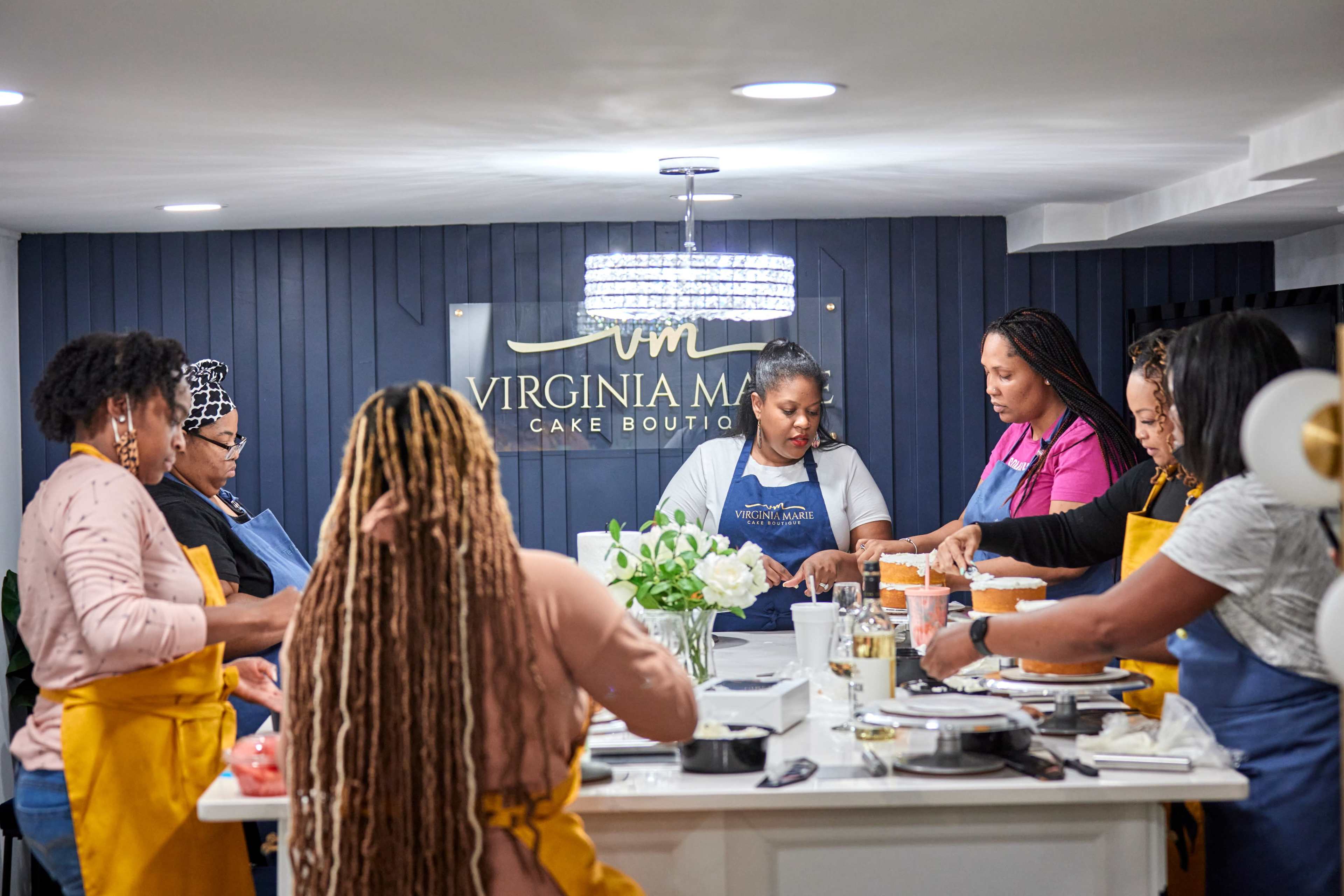 A group of women work together around a kitchen island, carefully decorating cakes in a cake boutique.