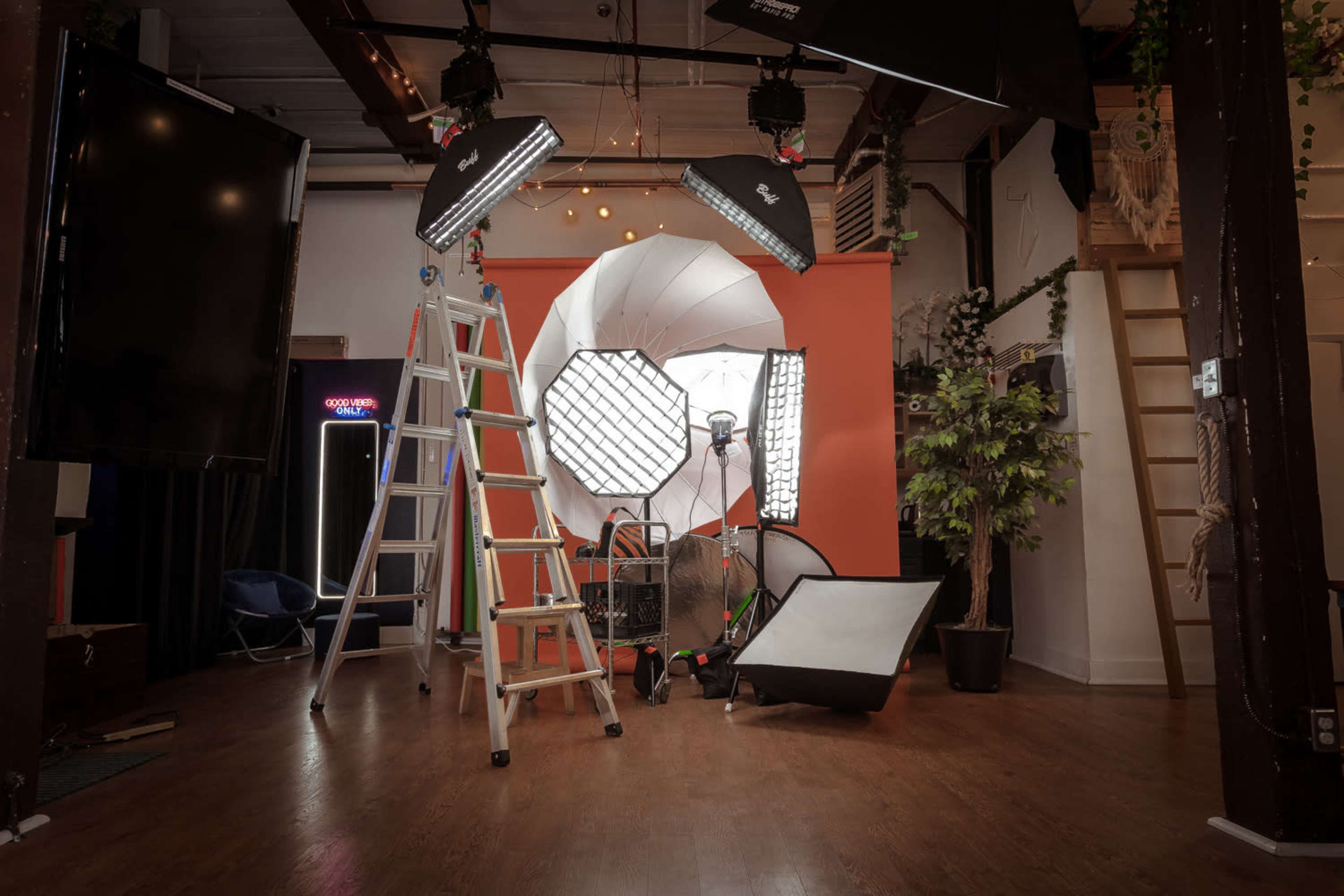 A photography studio equipped with various lighting setups, a ladder, and a backdrop.