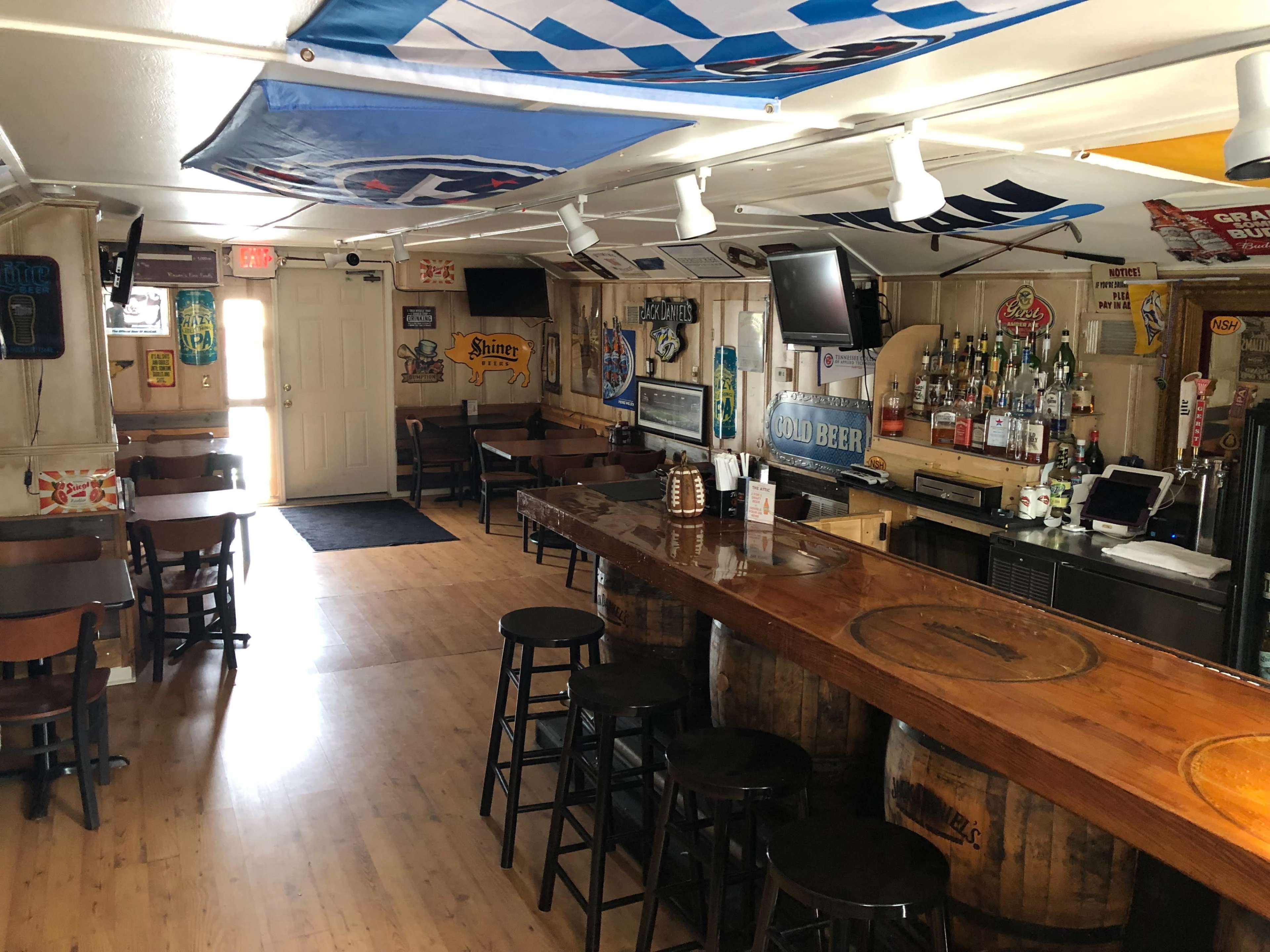 An empty bar with wooden stools, a polished counter, and various beer signs and memorabilia adorning the walls.