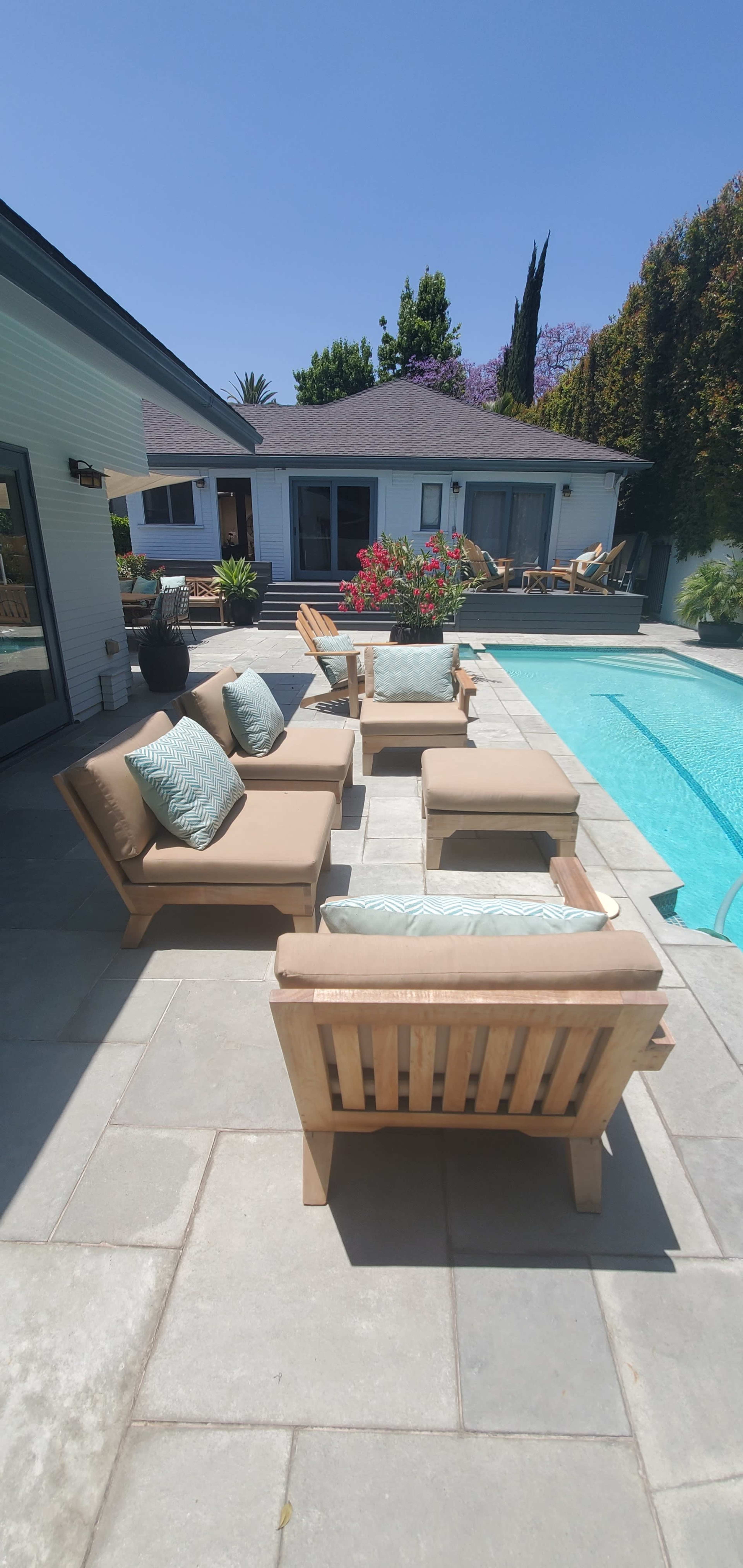 A serene poolside area with wooden lounge chairs and a clear blue pool surrounded by flowering plants.