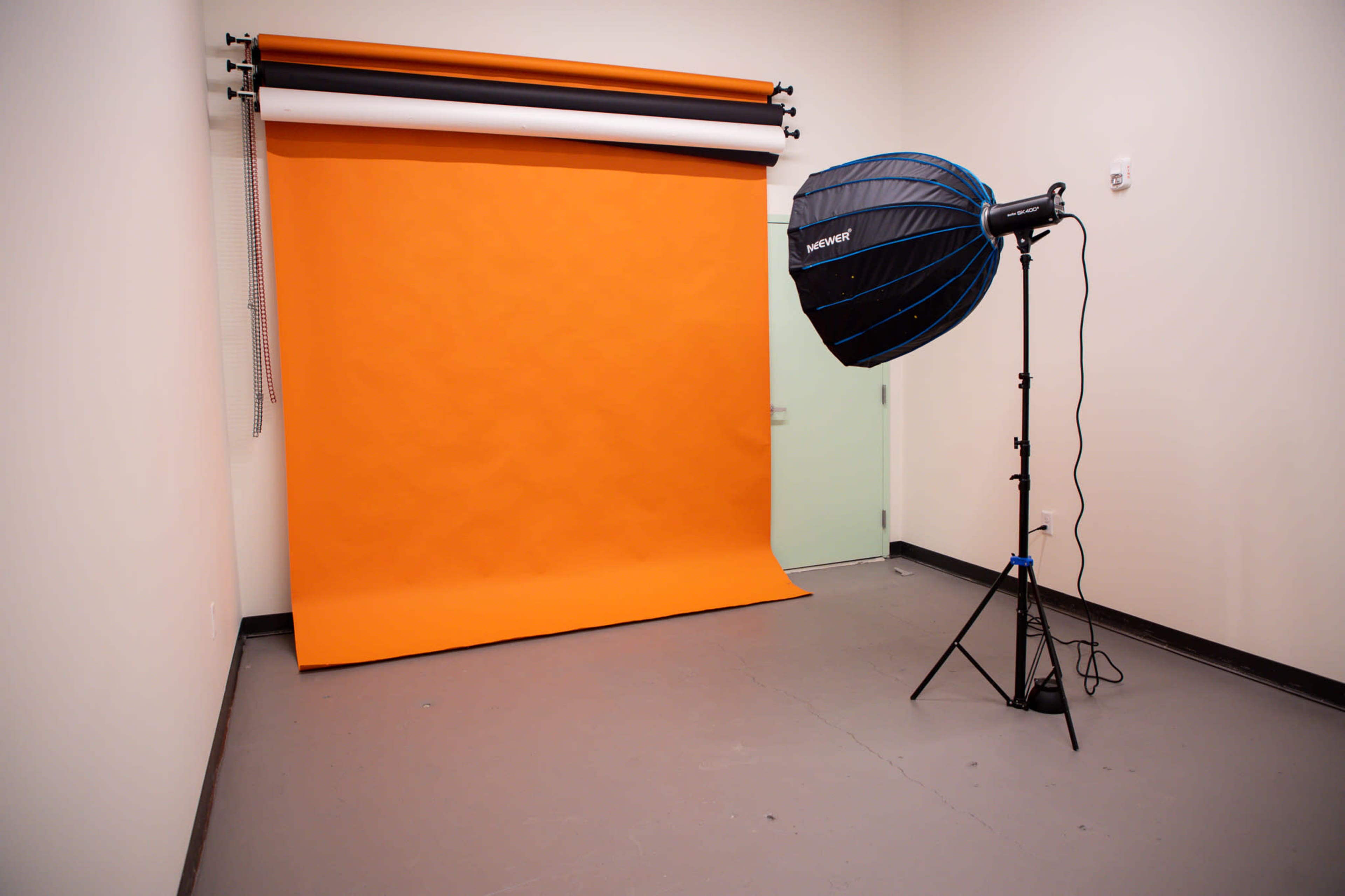 A studio setup with an orange backdrop and a large softbox light on a stand.