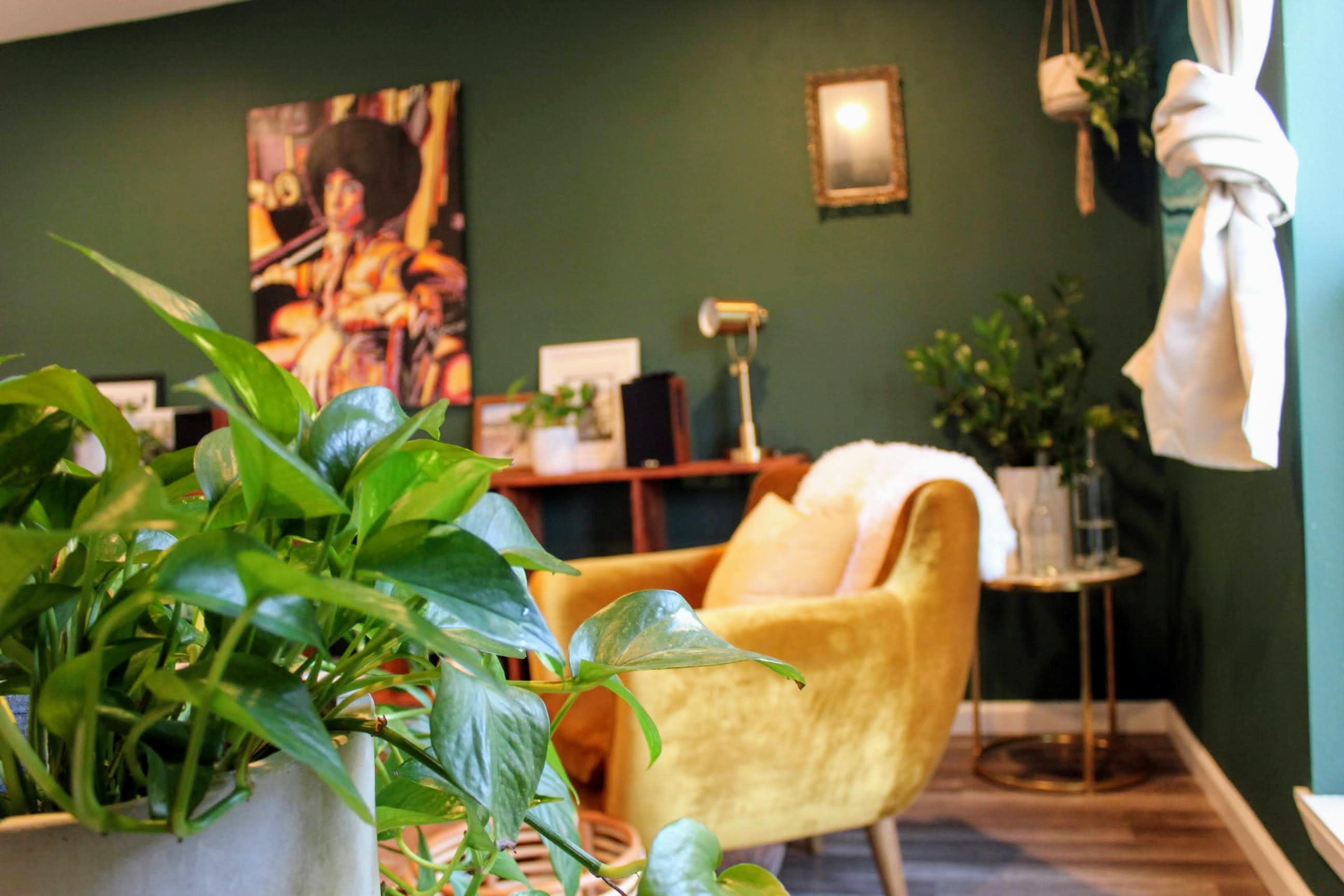 A cozy interior space with a green wall, a yellow armchair, a small table, and decorative plants.
