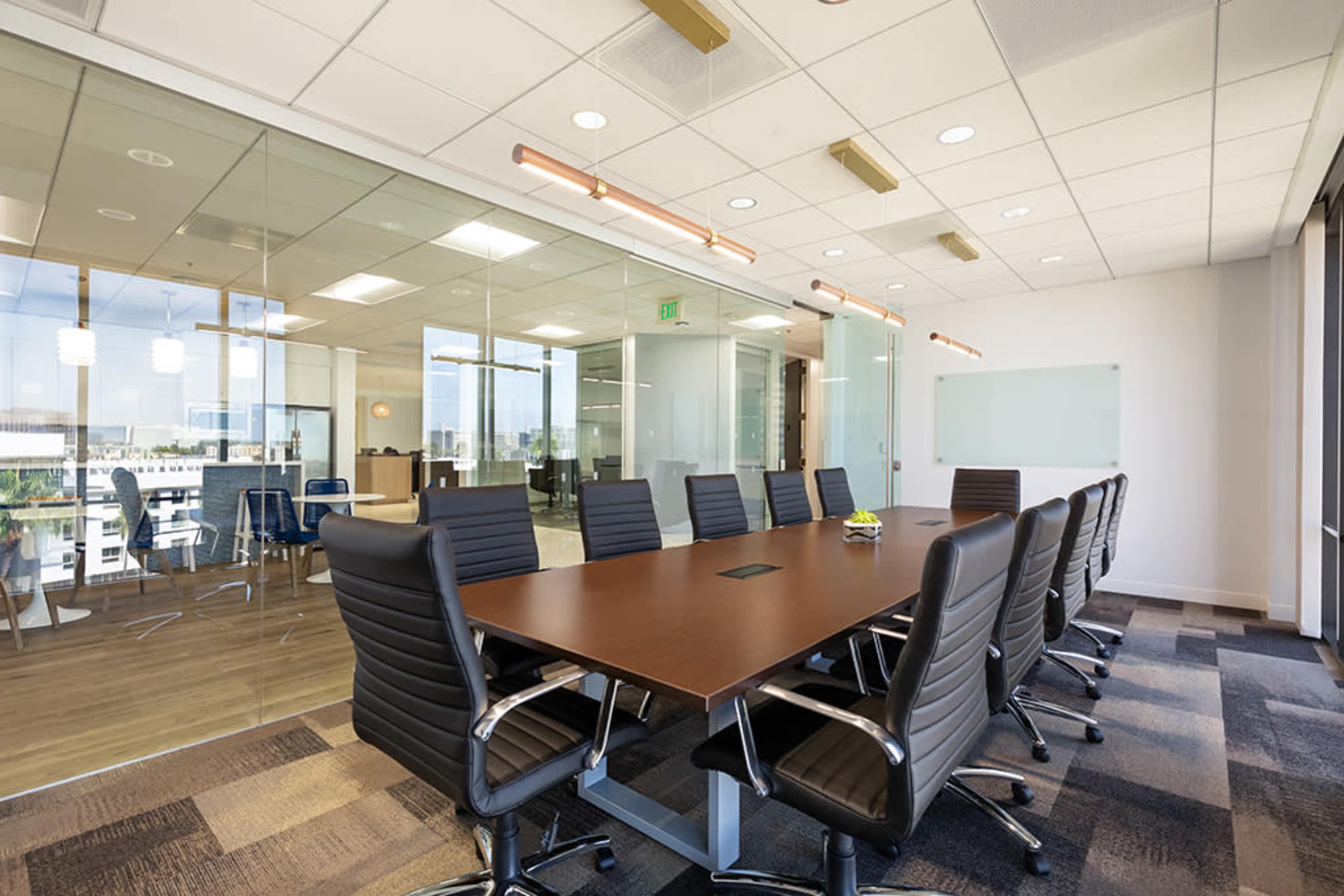 A large conference room features a wooden table surrounded by ergonomic black chairs, with glass walls revealing an adjacent workspace.