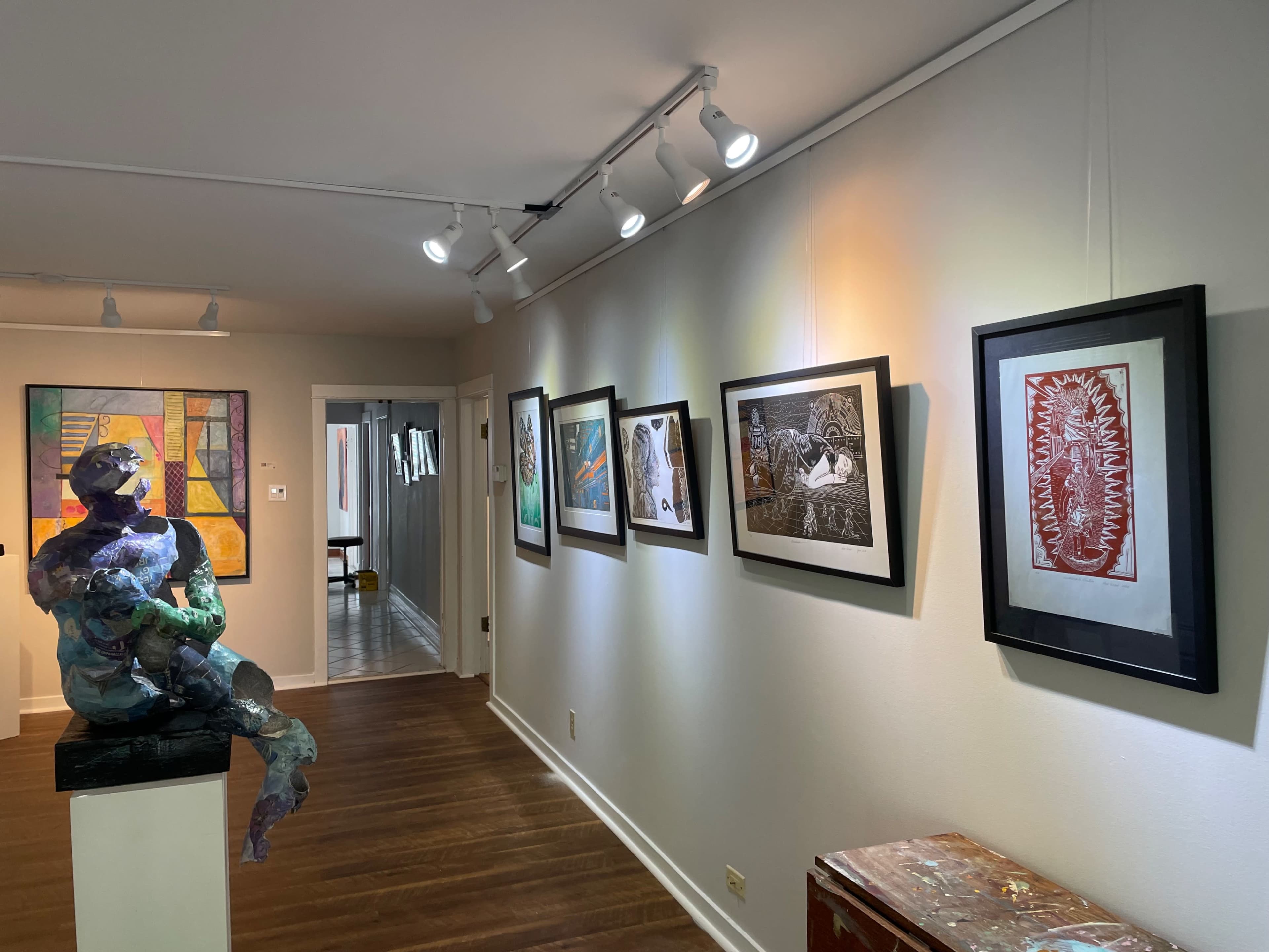 An art gallery featuring a colorful sculpture on a pedestal and a series of framed artworks displayed along the wall.