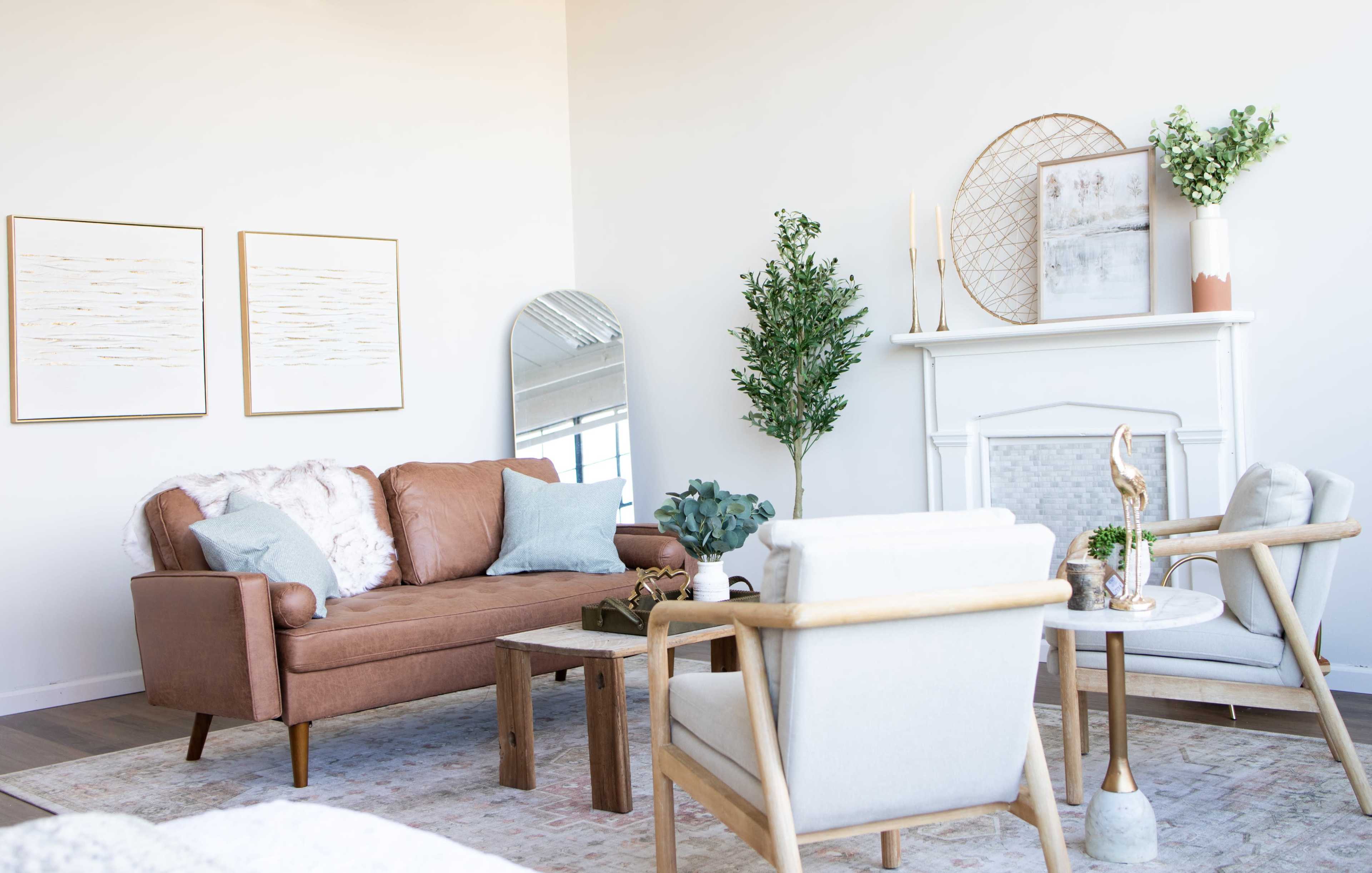 A modern living room featuring a brown couch, two light-colored armchairs, a wooden coffee table, and decorative elements like framed artwork and indoor plants.