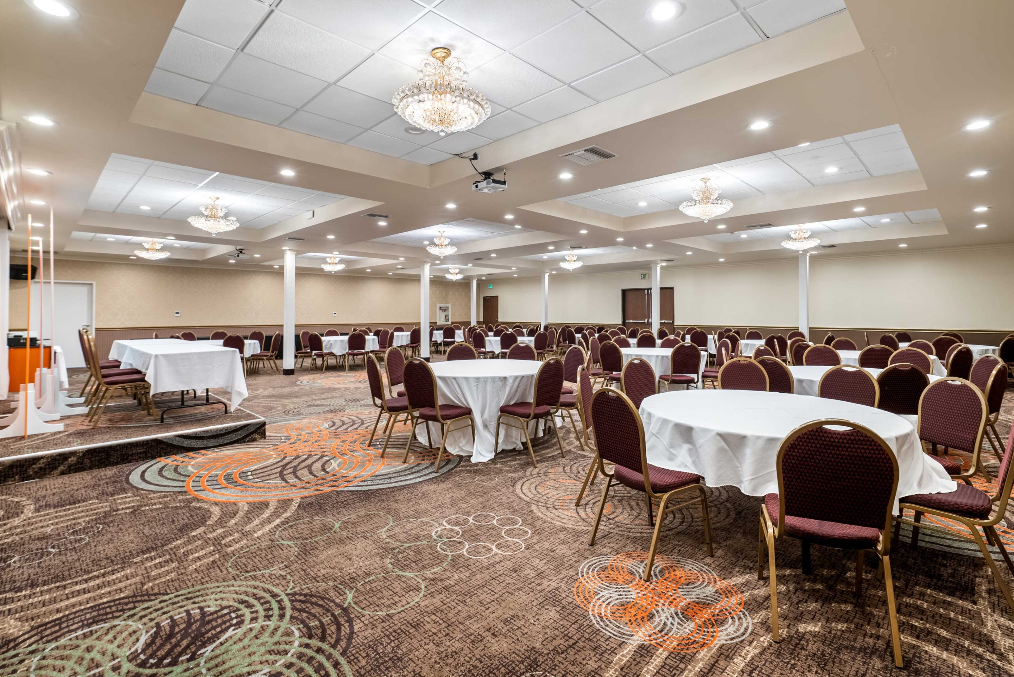 A banquet room with round tables covered in white tablecloths, surrounded by maroon chairs, and adorned with chandelier lighting.