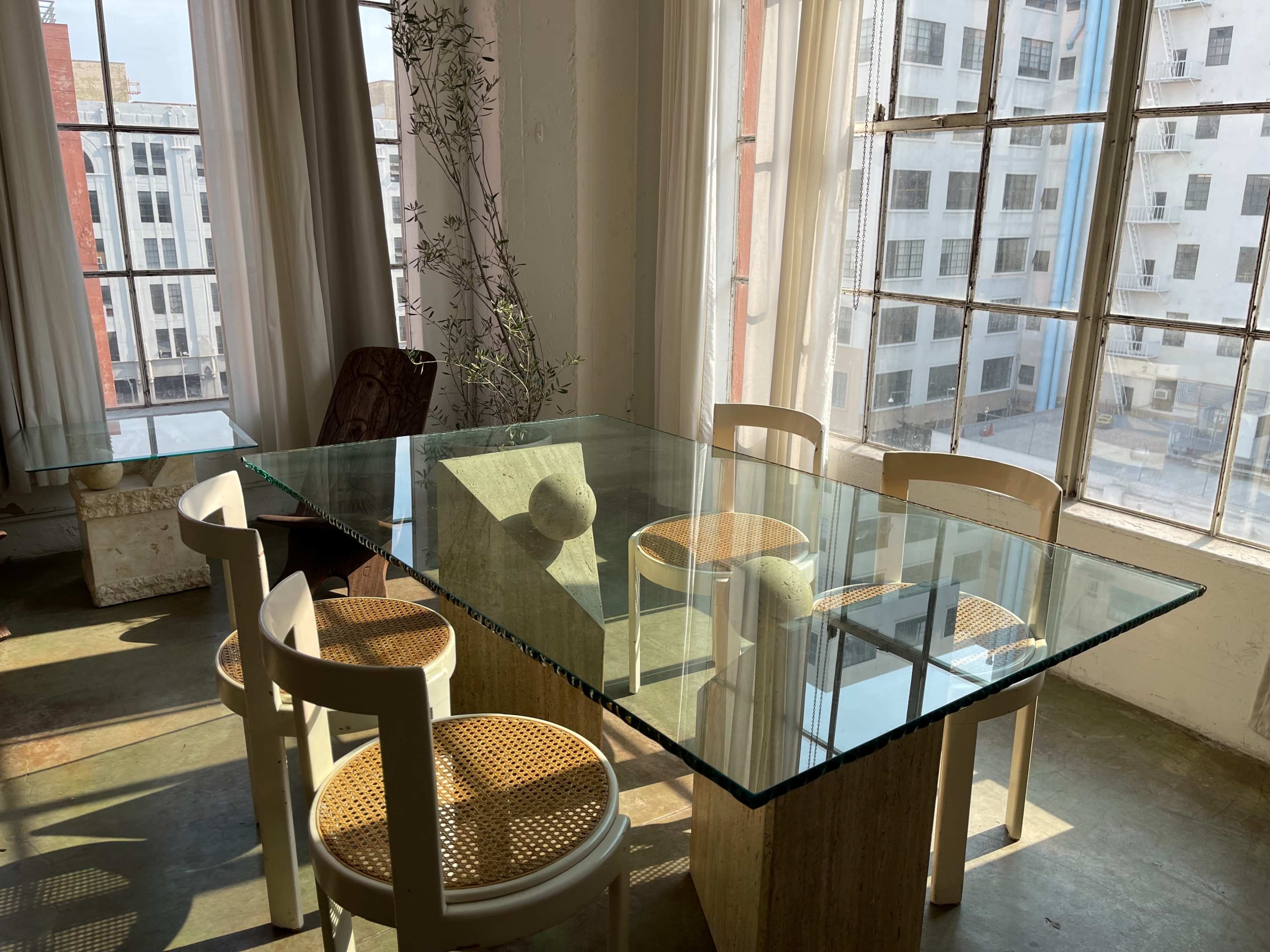 A glass-top table surrounded by four chairs is positioned near a large window overlooking a cityscape.
