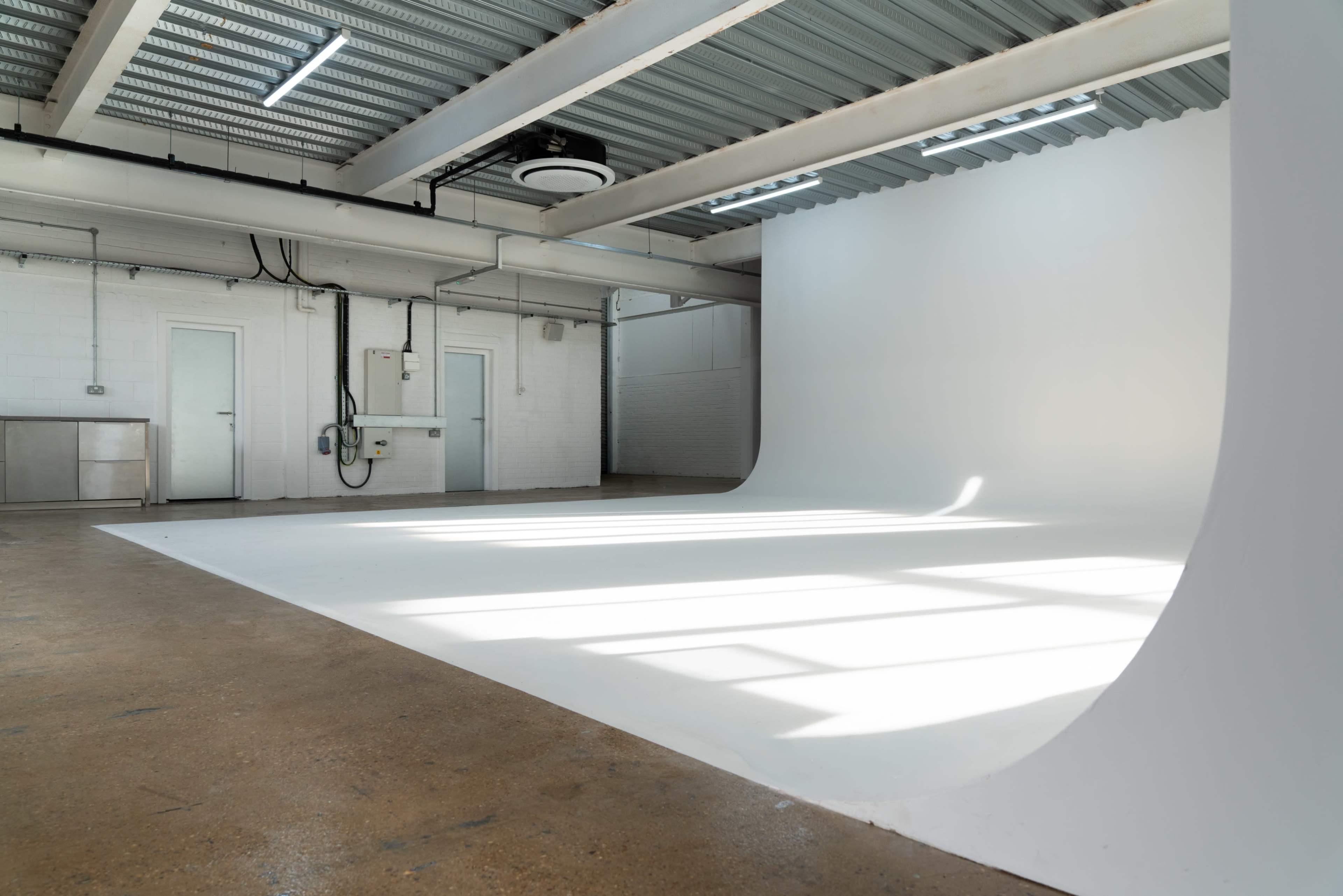The image shows a spacious, well-lit studio with a seamless white backdrop and a smooth floor.