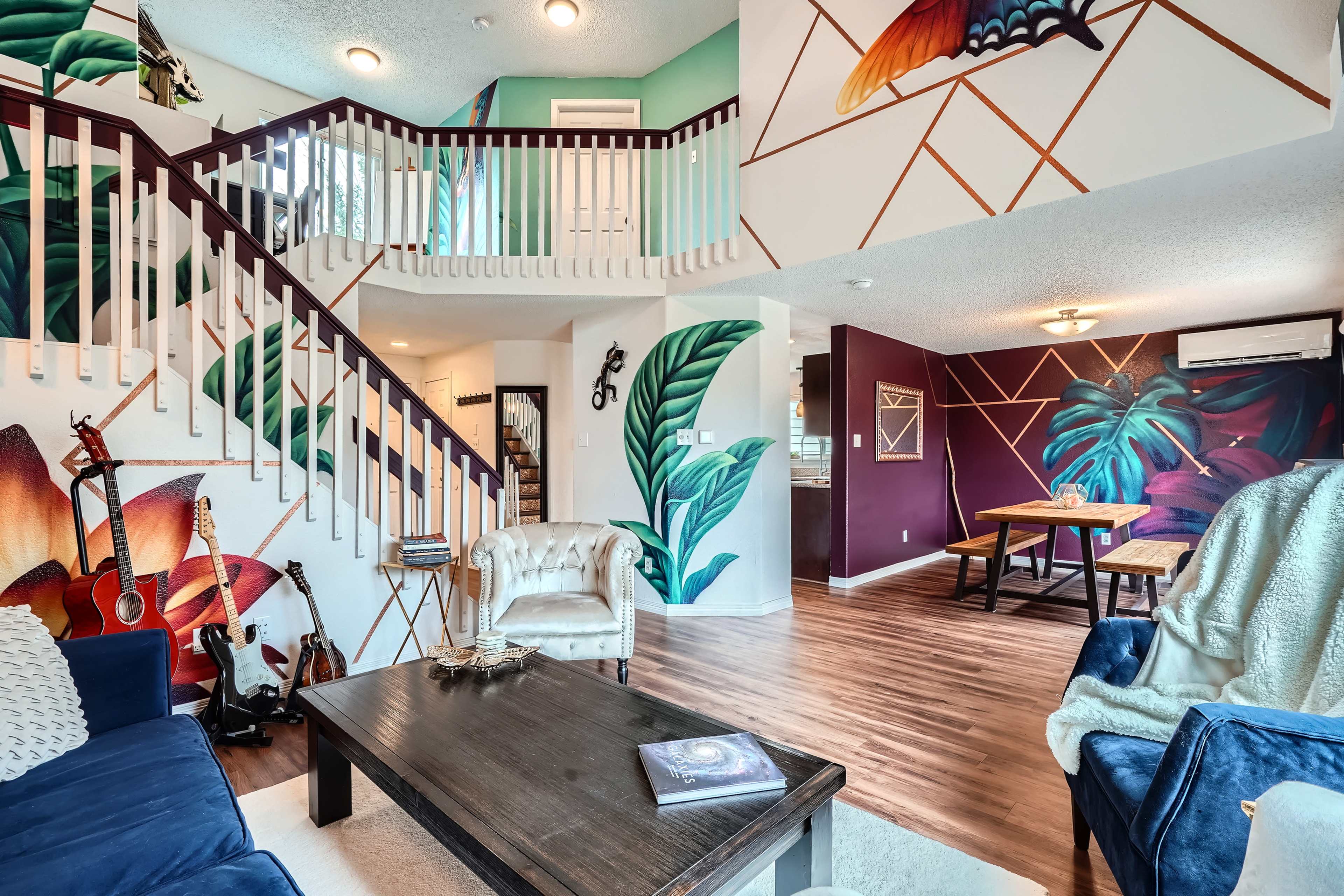 A multi-level living space with vibrant wall murals, a staircase, and a seating area featuring a coffee table and guitar.
