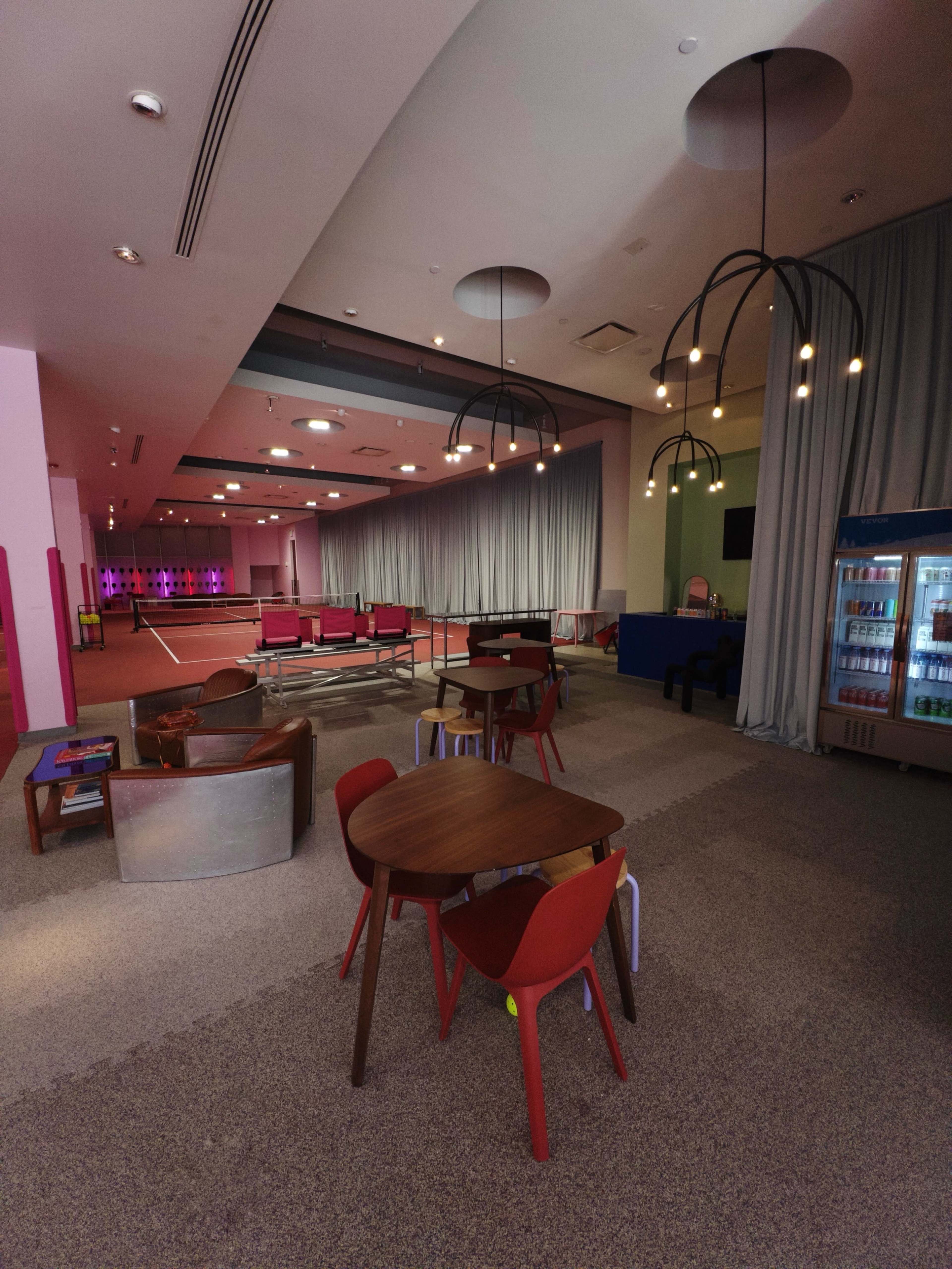 A modern lounge area with colorful furniture, including tables and chairs, and illuminated features in a spacious, partially curtained space.