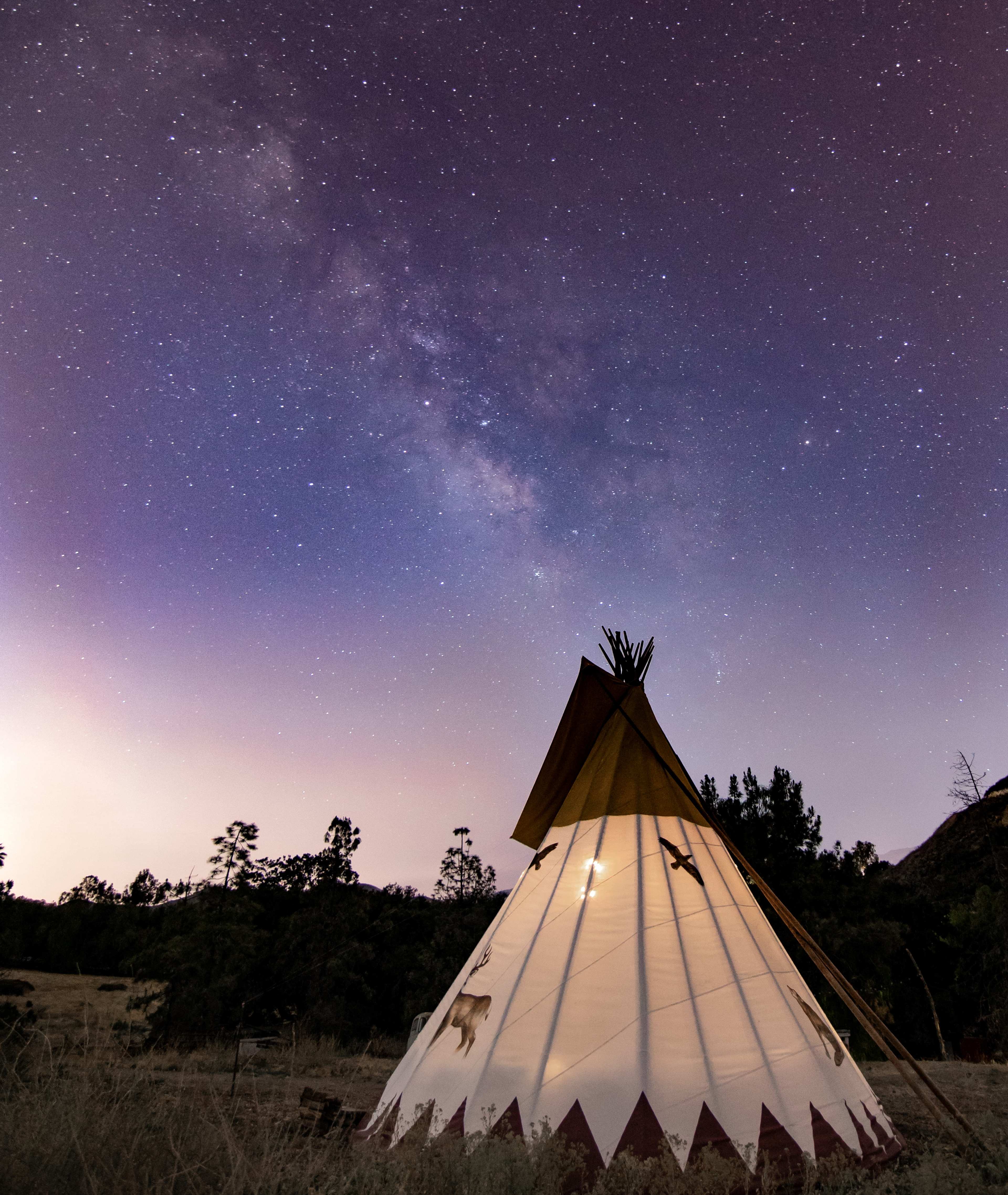 A illuminated teepee stands under a starry night sky filled with the Milky Way.