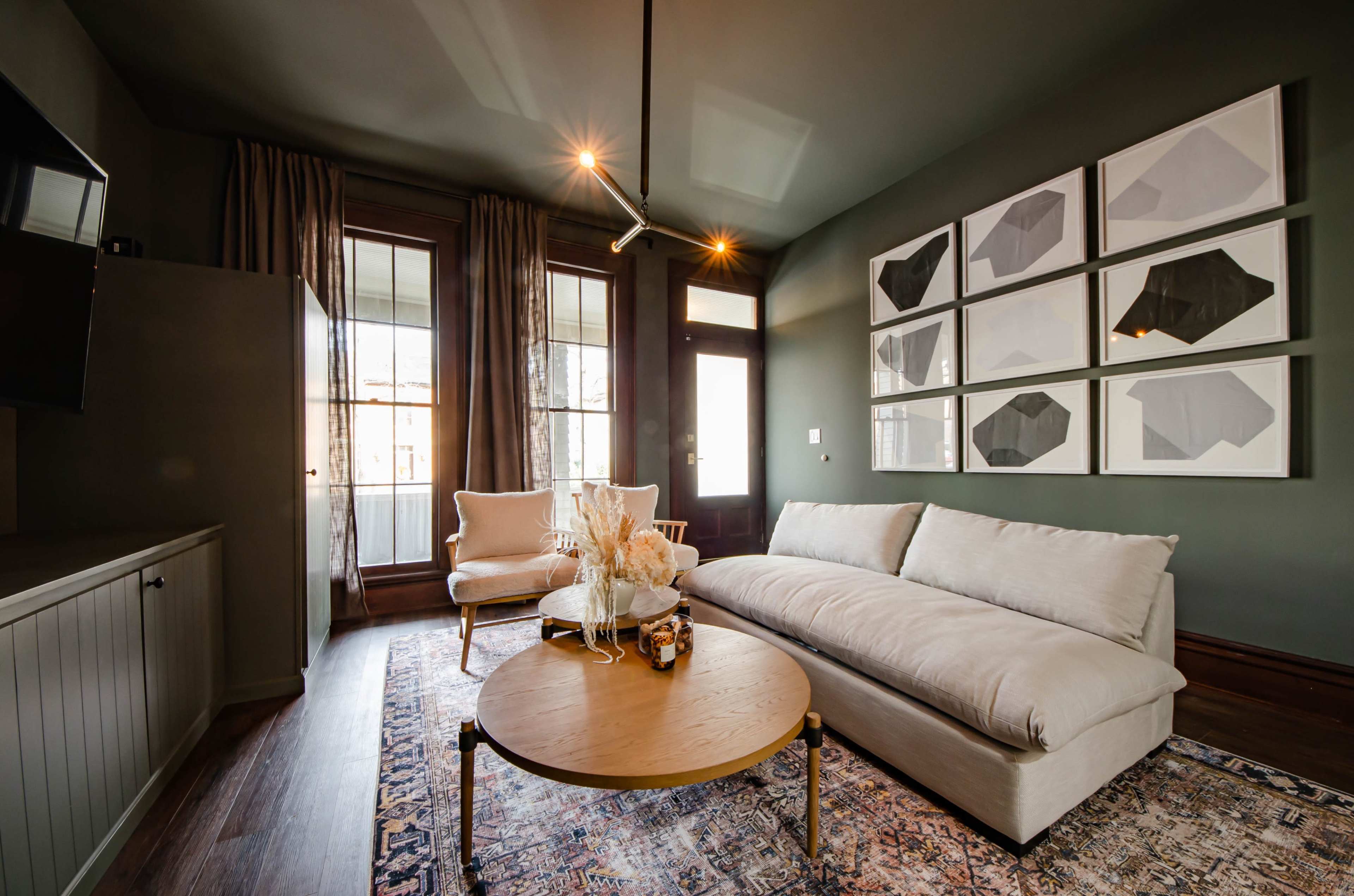 A modern living room with a beige sofa, a round wooden coffee table, and framed black-and-white artwork on the dark green walls.