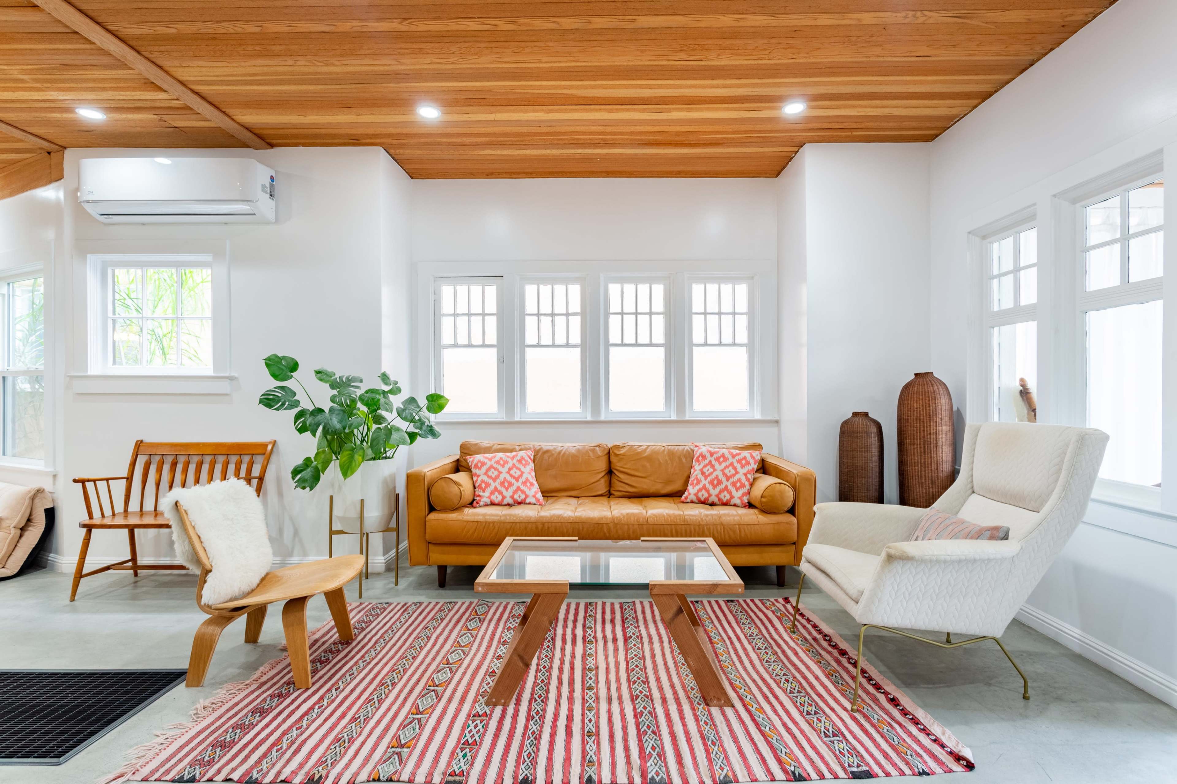 A bright living room featuring a brown leather sofa, a wooden coffee table, and a patterned rug, with large windows allowing natural light to fill the space.