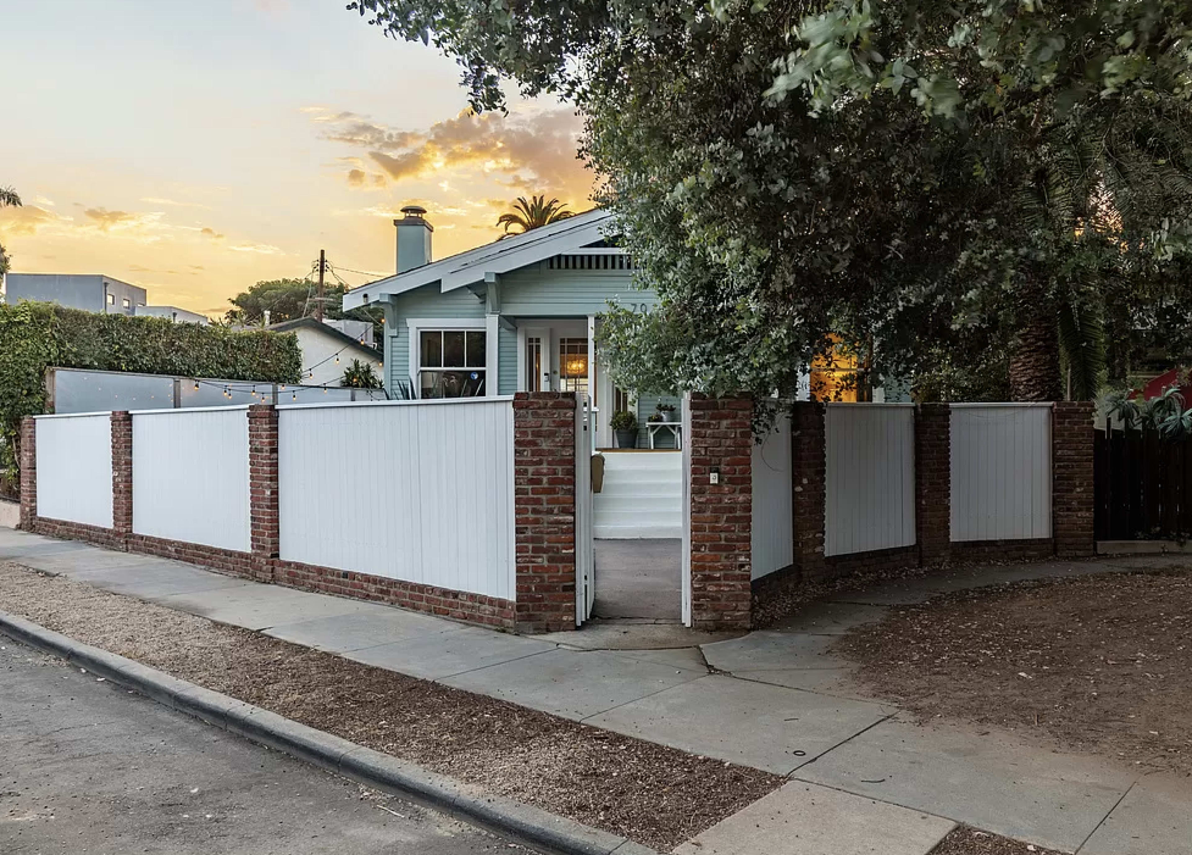 A light blue house with a brick and white fence is set against a twilight sky.
