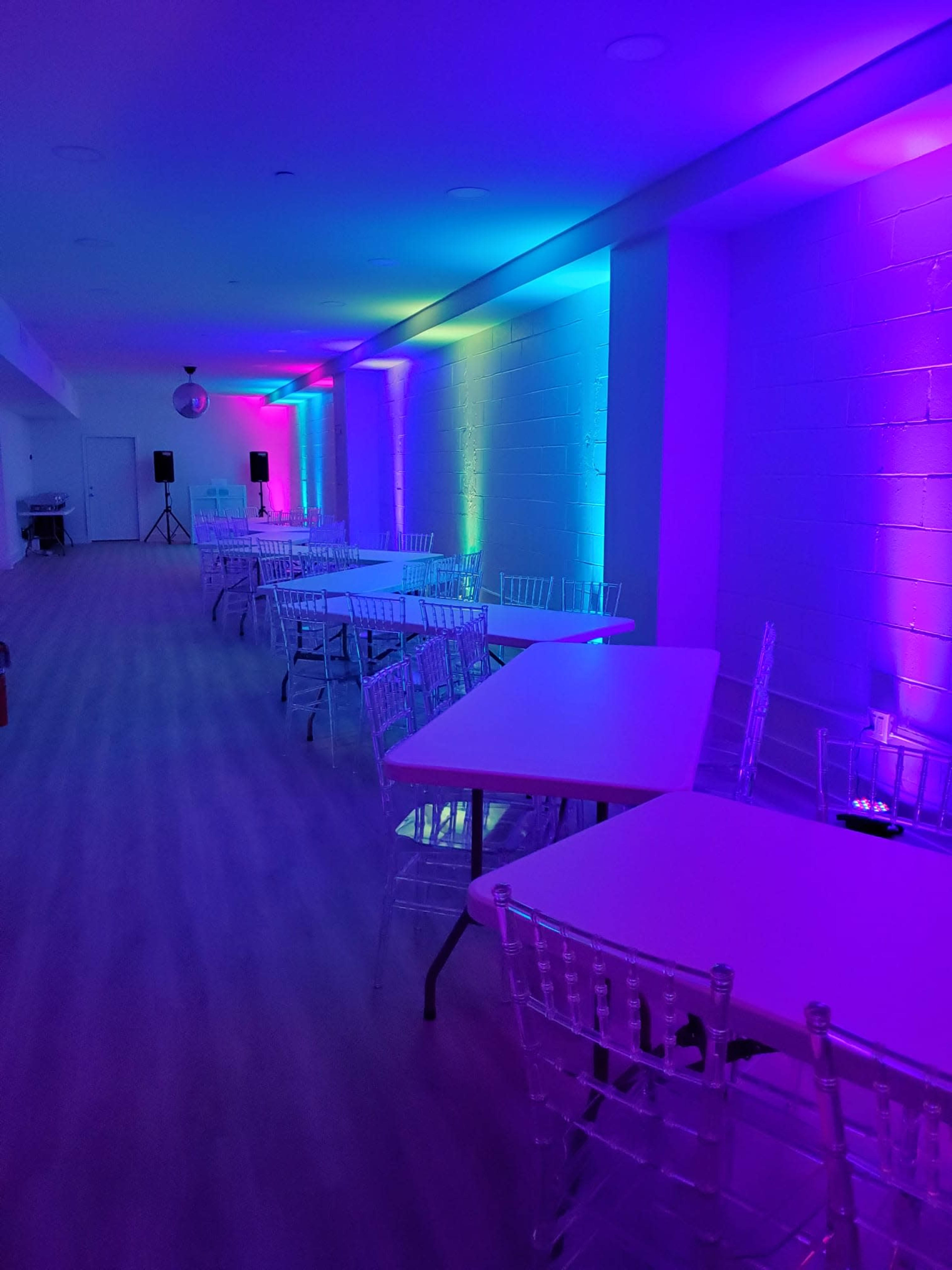The image shows a well-lit event space with multiple rows of tables and chairs, featuring purple and blue ambient lighting along the walls.