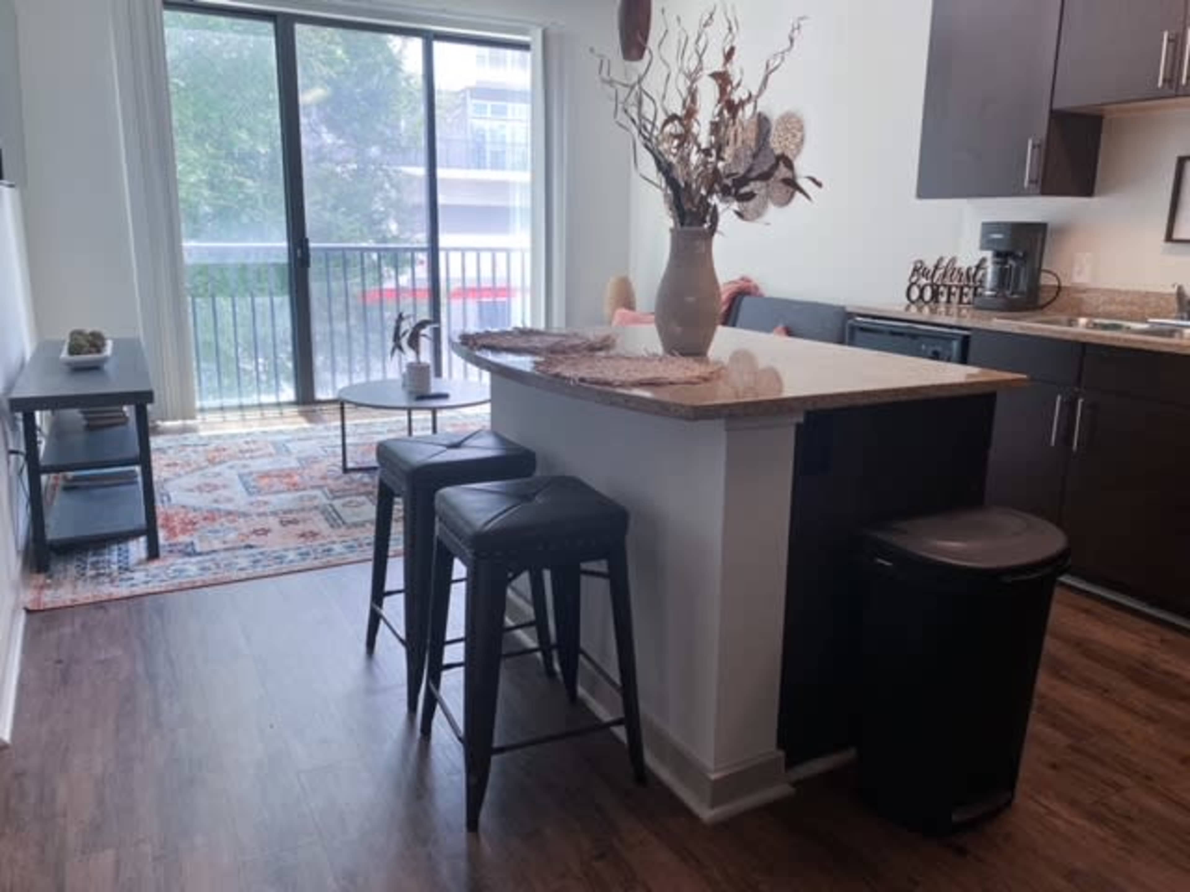 A kitchen area features a bar with three stools, a decorative vase on the countertop, and a sliding glass door leading to a balcony.
