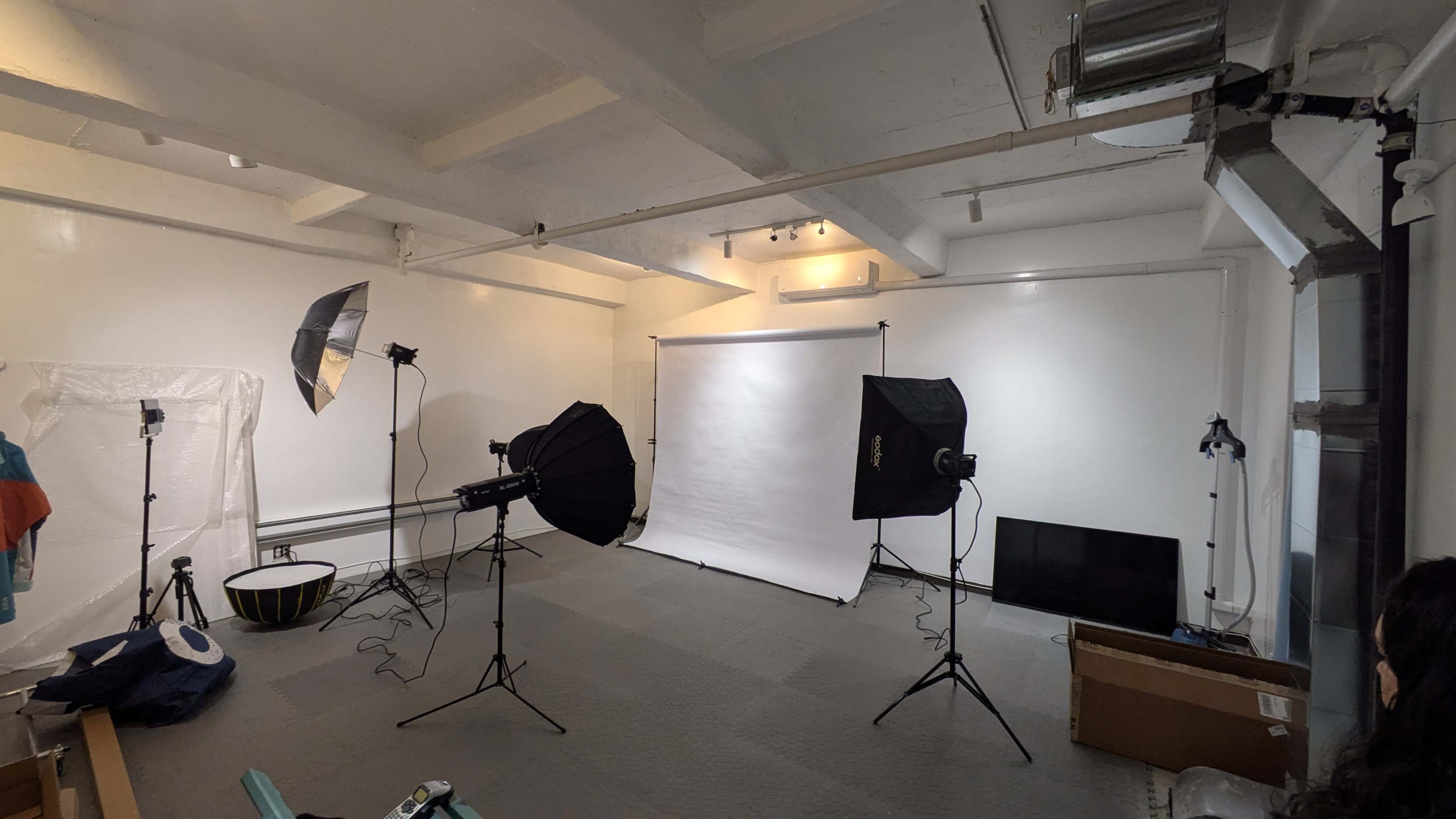 The image shows a photography studio equipped with several light sources, a backdrop, and various props organized around the space.