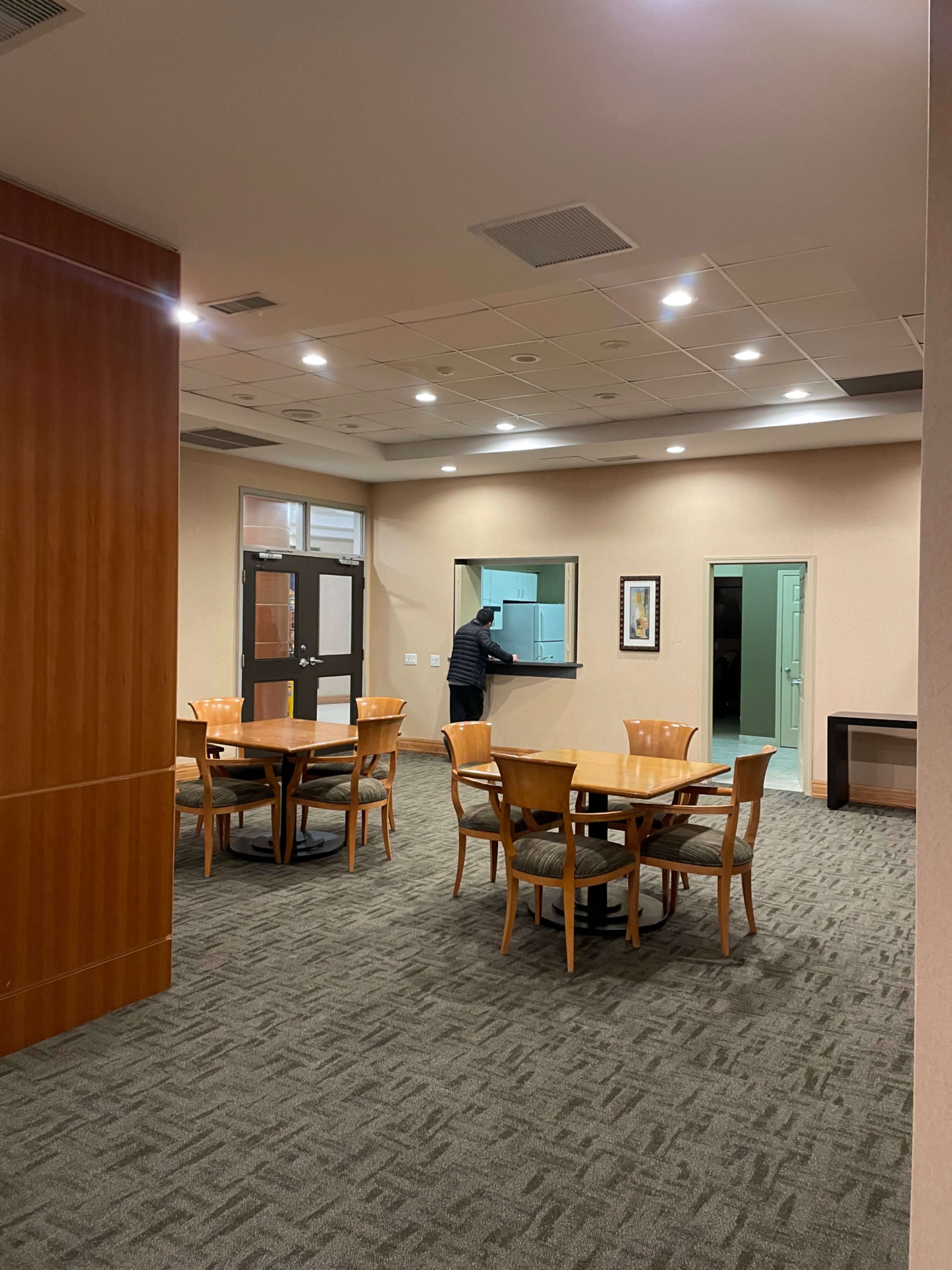 A person stands at a service counter in a room with several tables and chairs arranged for seating.