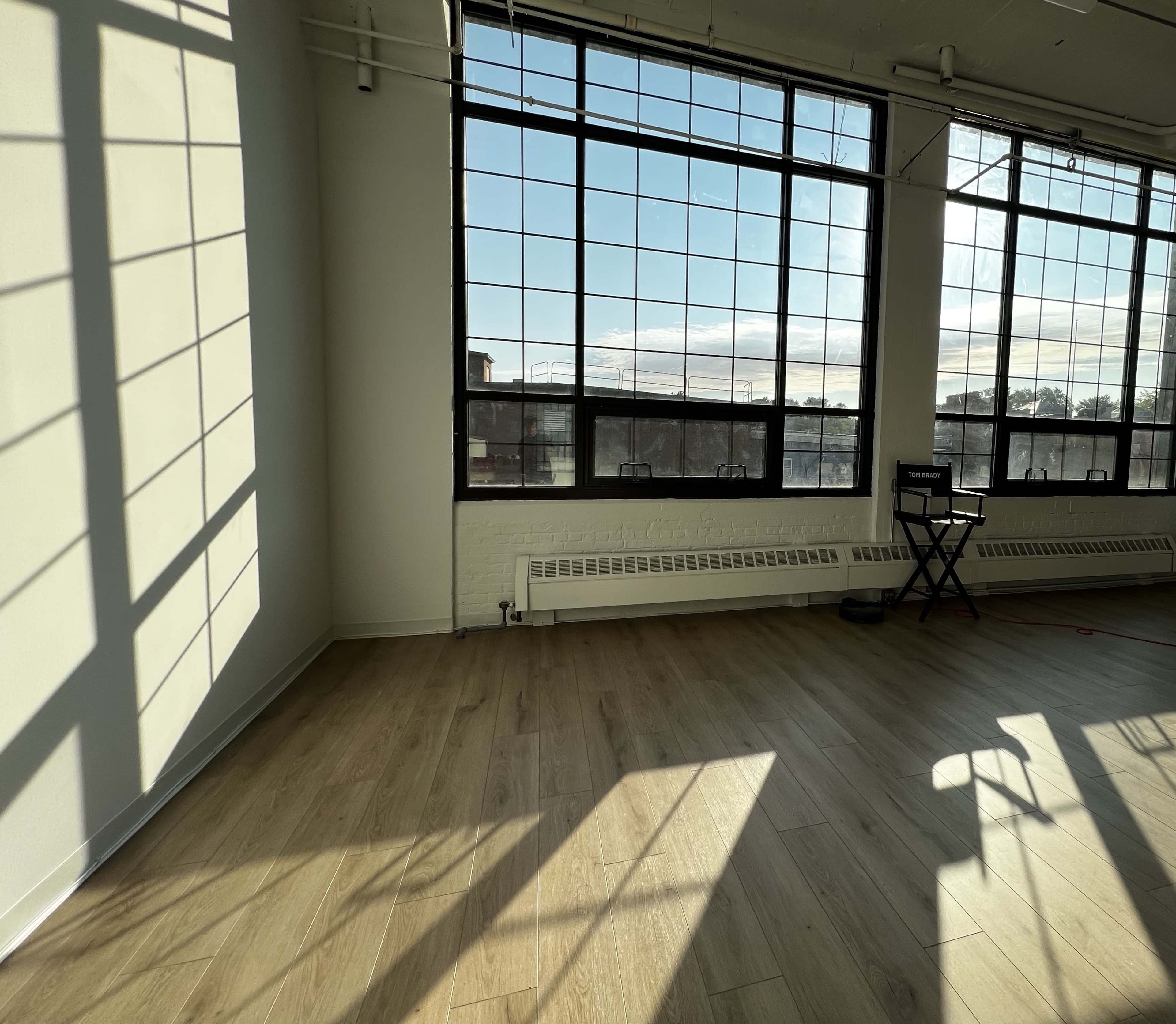 A spacious room with large windows casting shadows on the wooden floor.