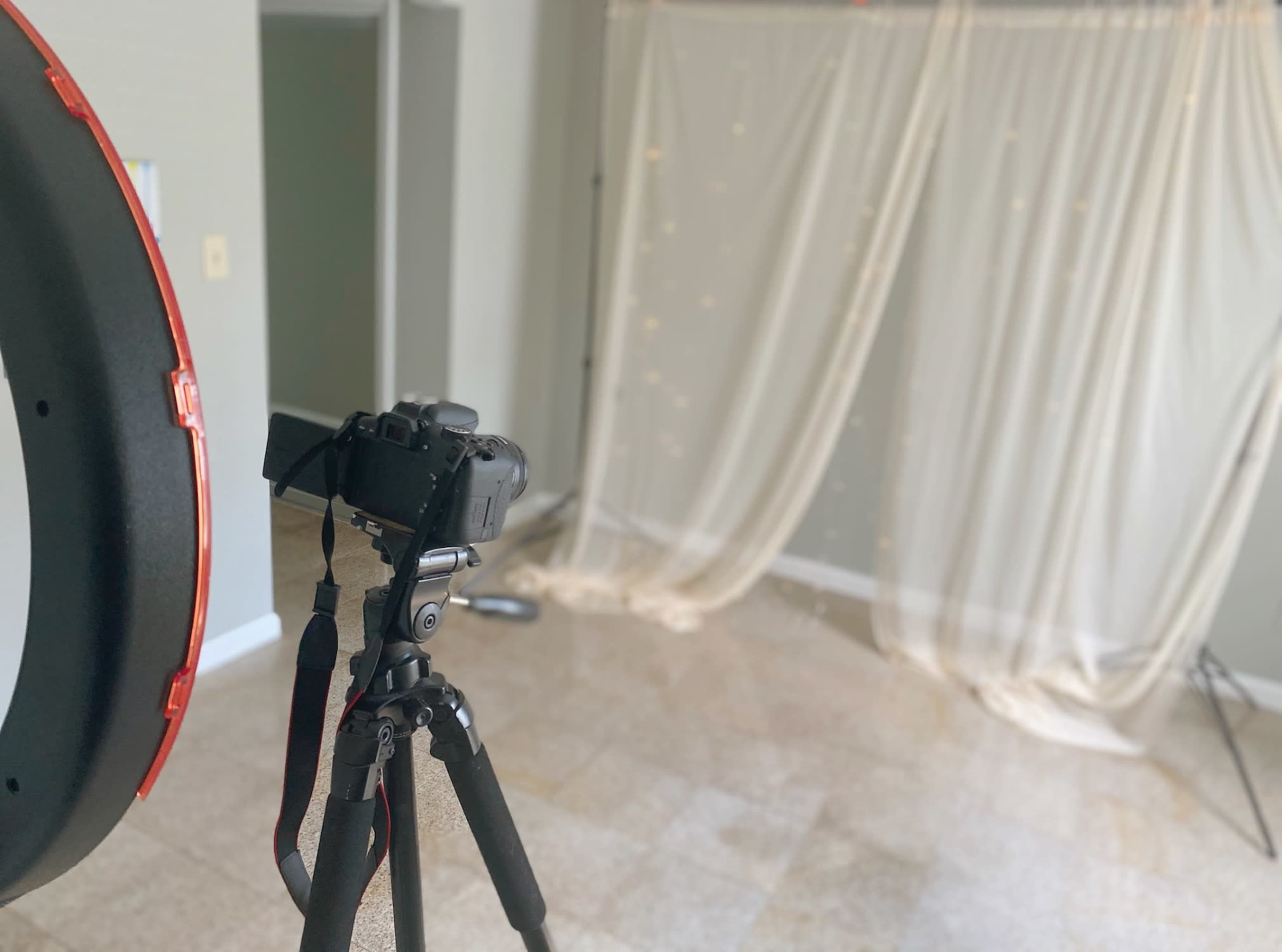 A camera on a tripod is set up facing a fabric backdrop with lights, ready for a photoshoot.