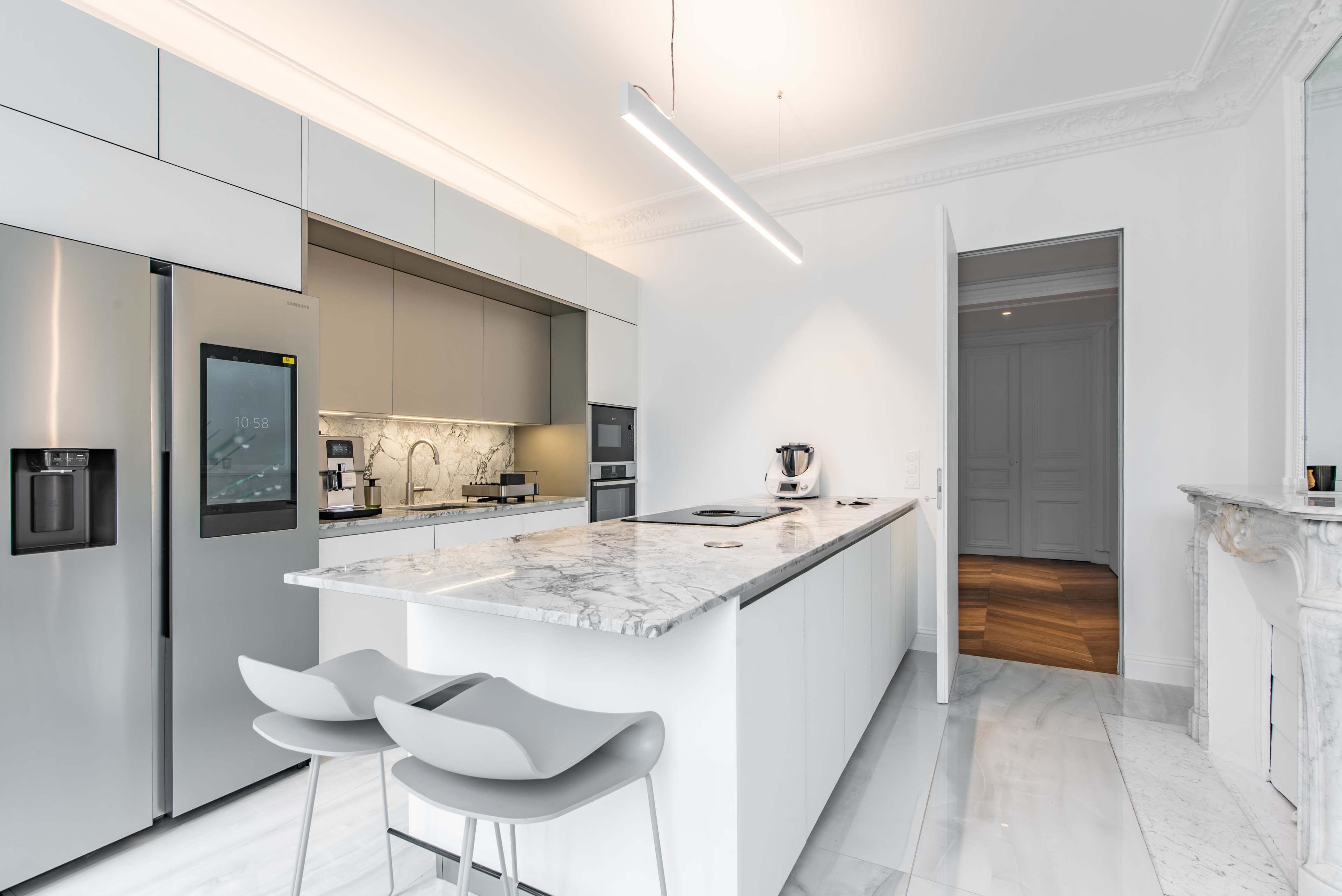 The image shows a modern kitchen with sleek cabinetry, a marble island, and stainless steel appliances, including a refrigerator and oven.