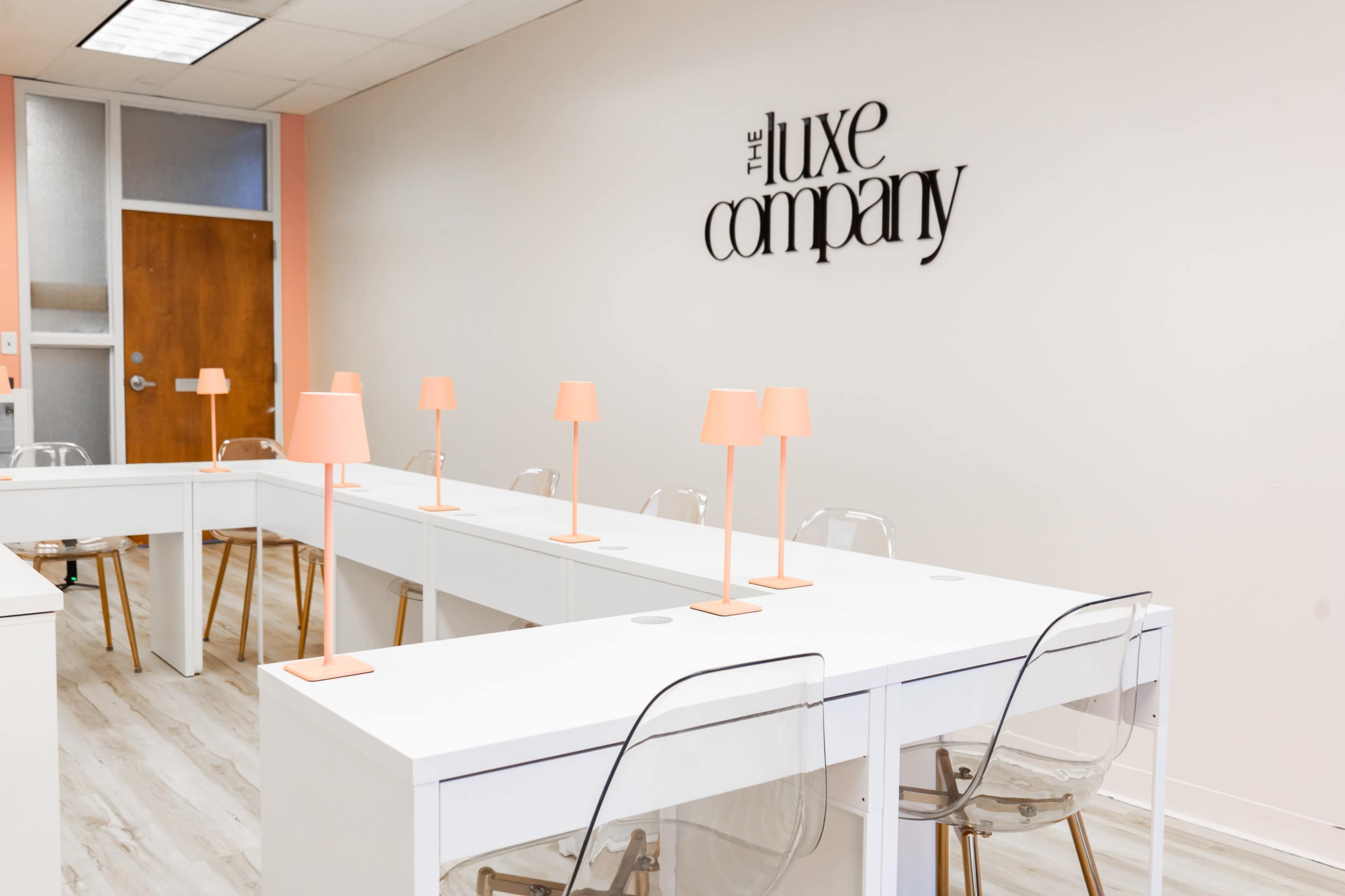 The image shows a modern, minimalist workspace with white tables, clear chairs, and peach-colored lamps arranged neatly in a well-lit room.