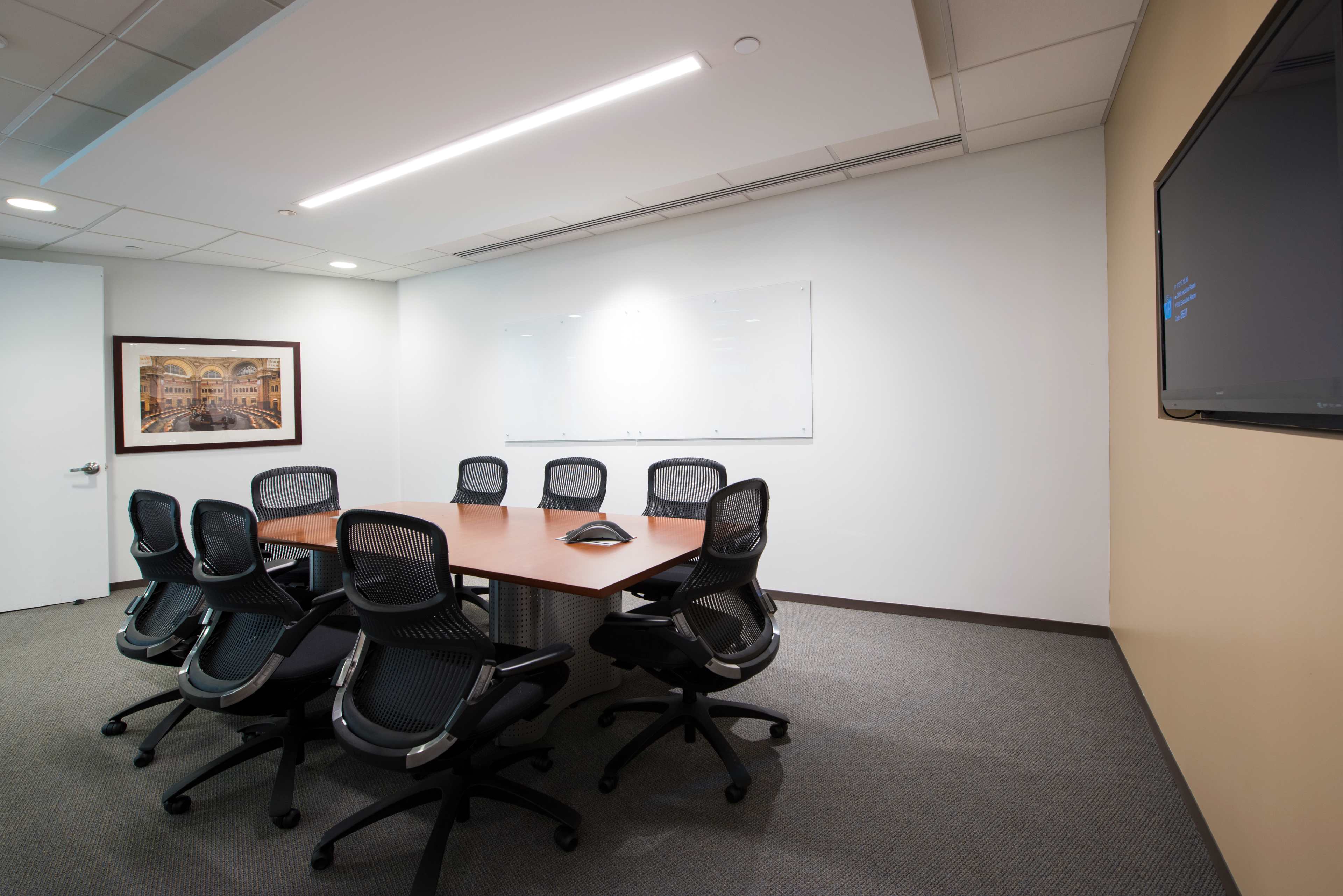 A modern conference room features a rectangular table surrounded by ergonomic chairs, a wall-mounted television, and a whiteboard.
