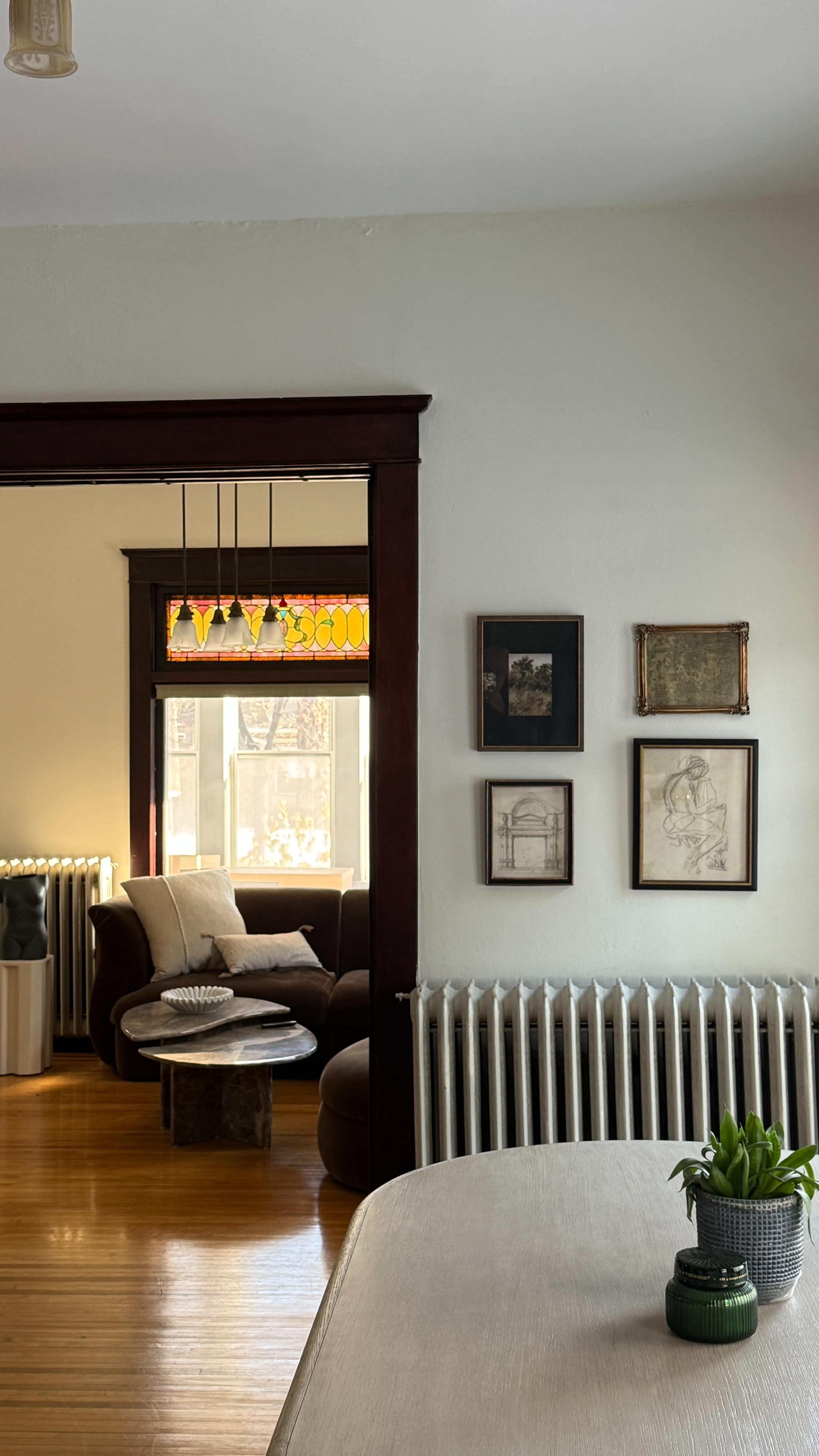 The image shows a cozy living space featuring a brown couch, art on the walls, and a decorative table with a plant in the foreground.