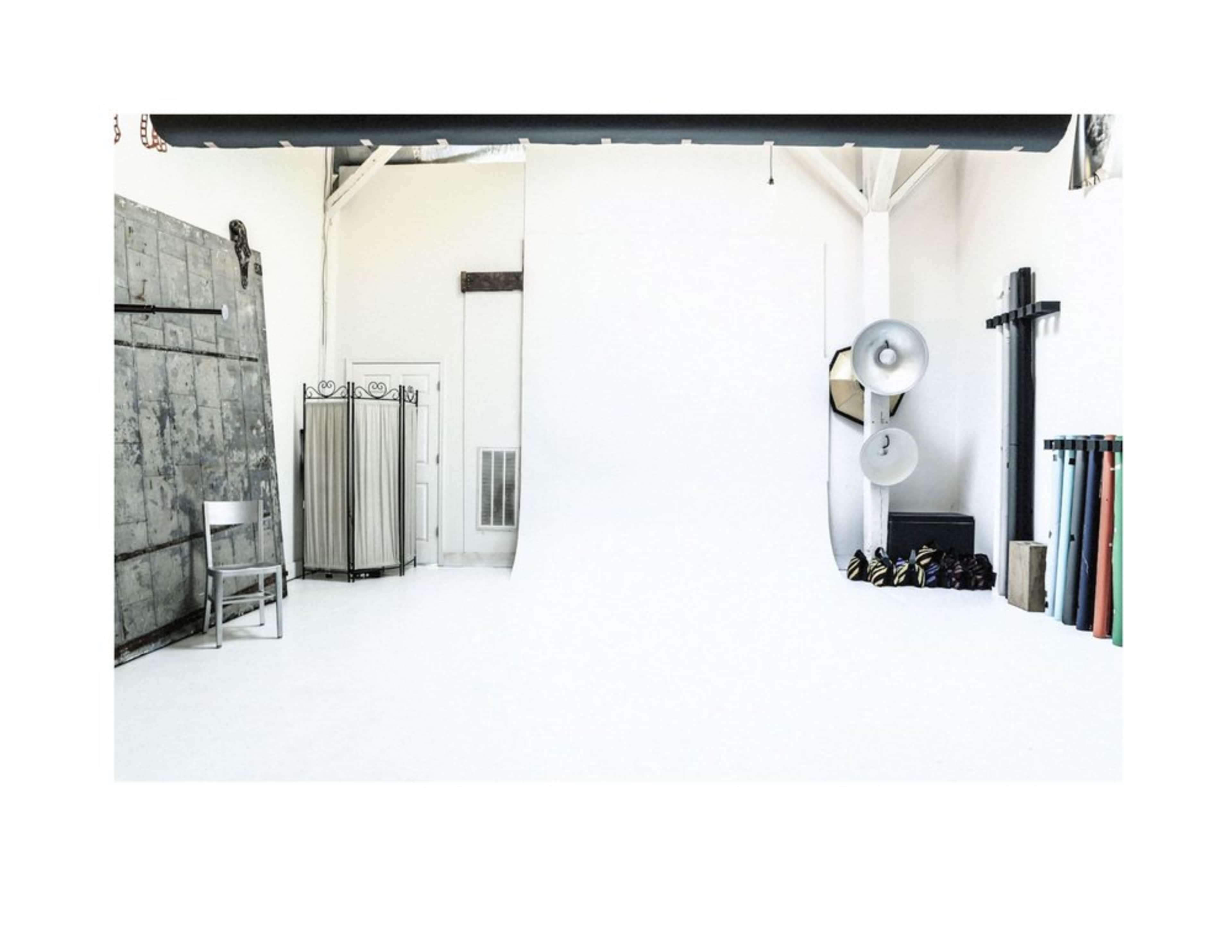 The image shows a spacious, minimalist photography studio with a white backdrop and various equipment along the walls.